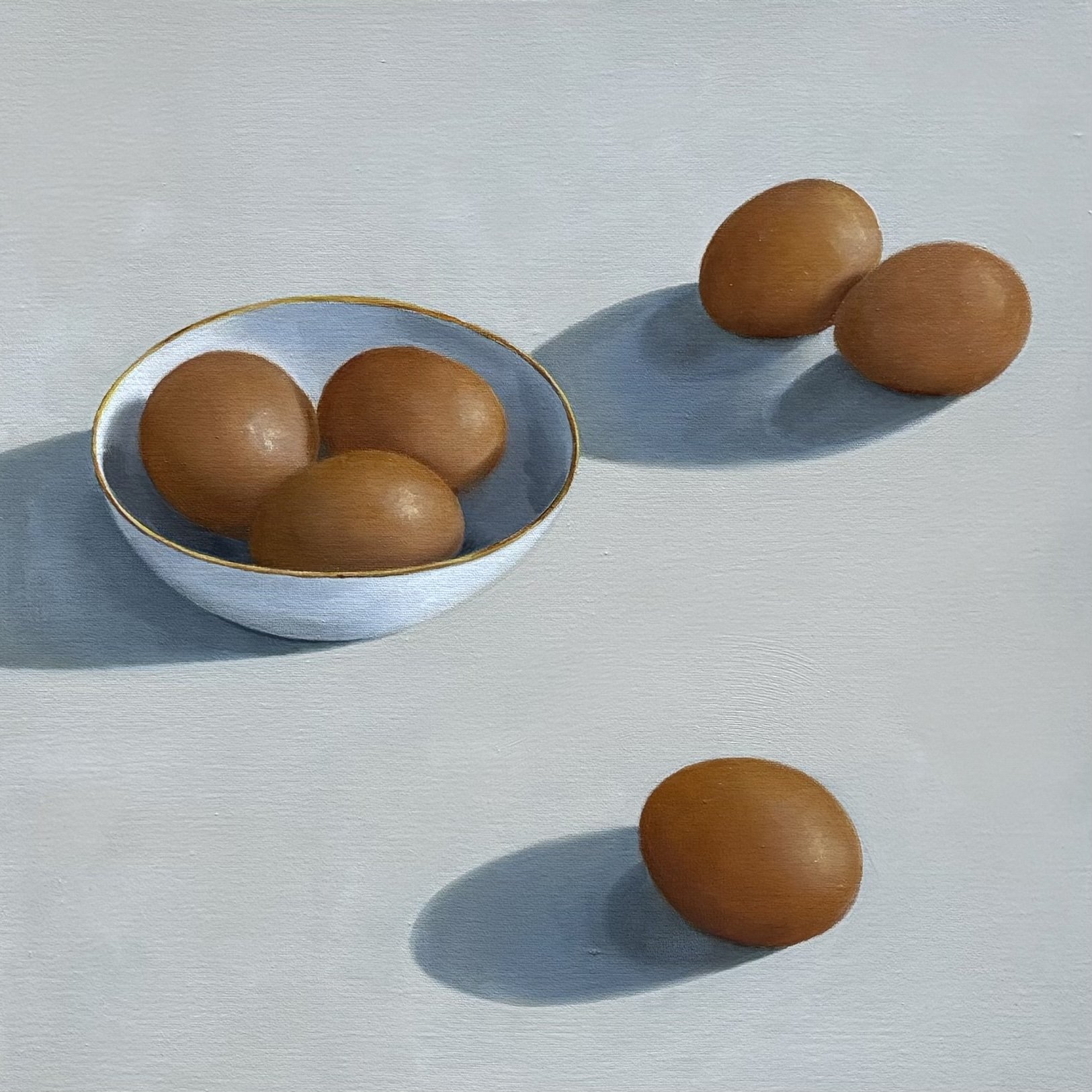 Four brown eggs, three in a white bowl with a gold rim and one on a white surface, casting shadows.