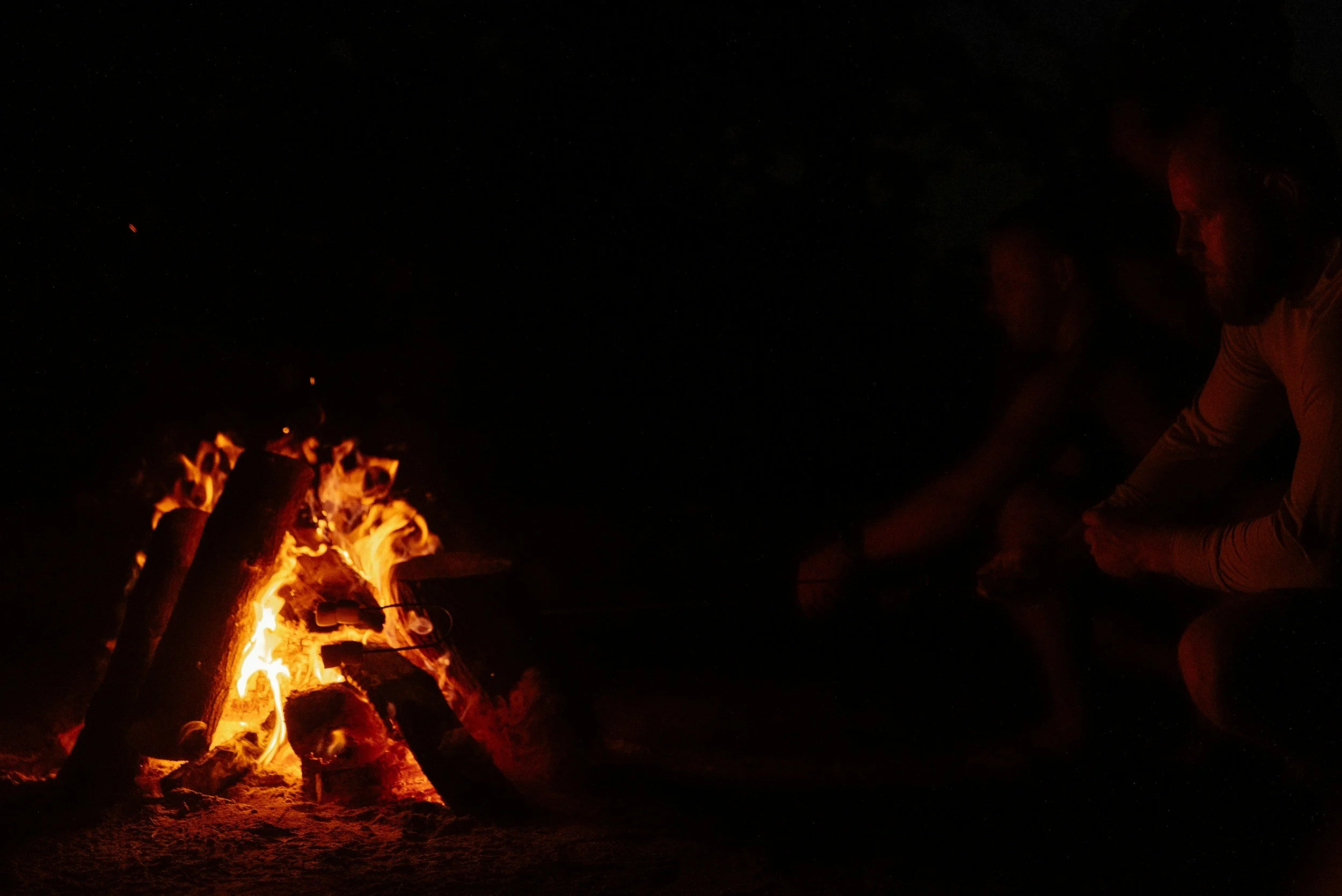 Twee mensen zitten rond een kampvuur in de nacht.