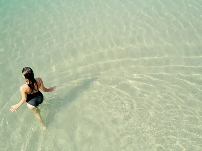 frau-im-schwarzen-badeanzug-geht-ins-klare-turkisfarbene-meer-an-einem-tropischen-strand.png
