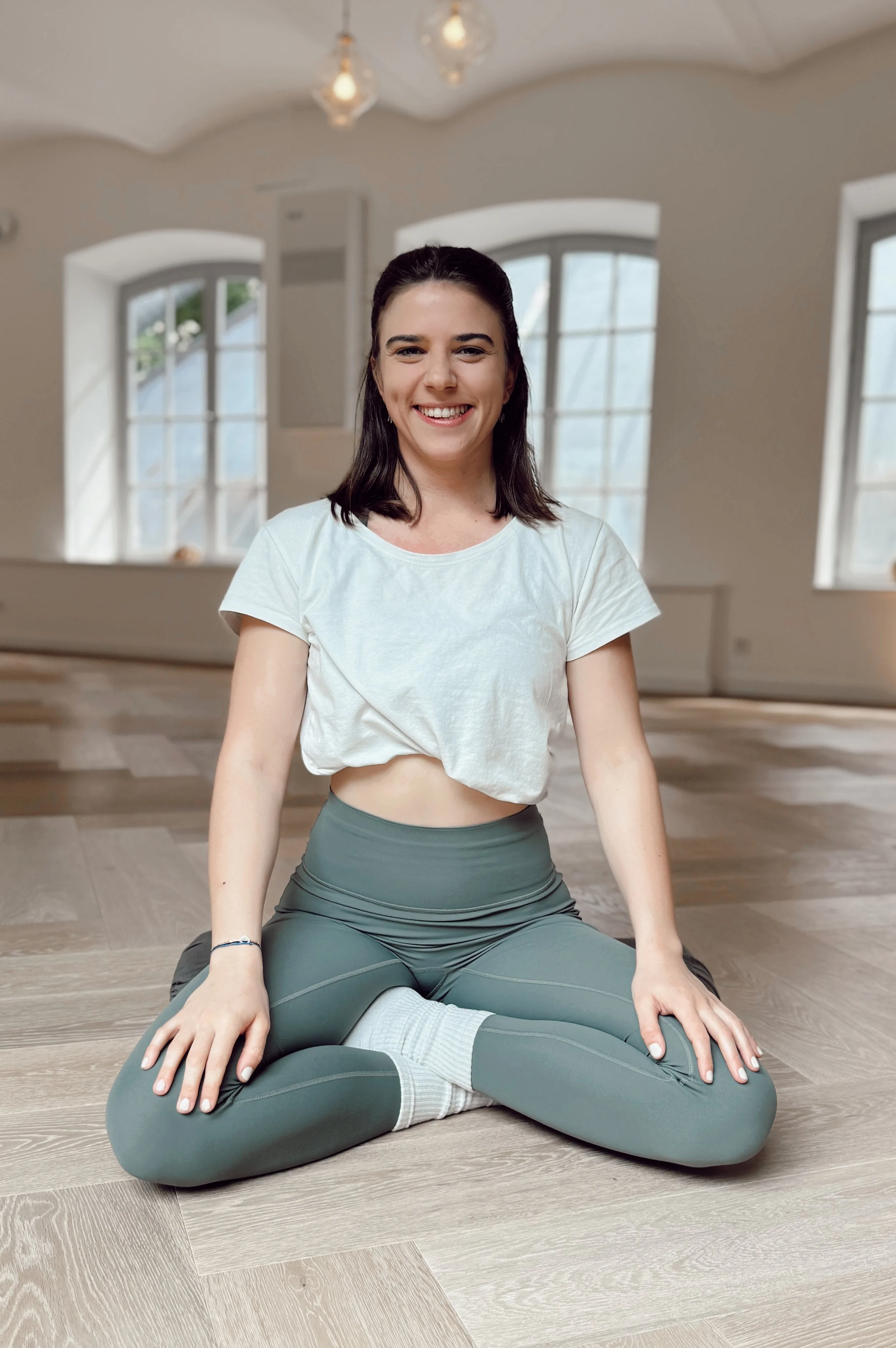 Junge Frau macht Yoga im Wohnzimmer, sitzt in Meditationpose auf dem Boden.