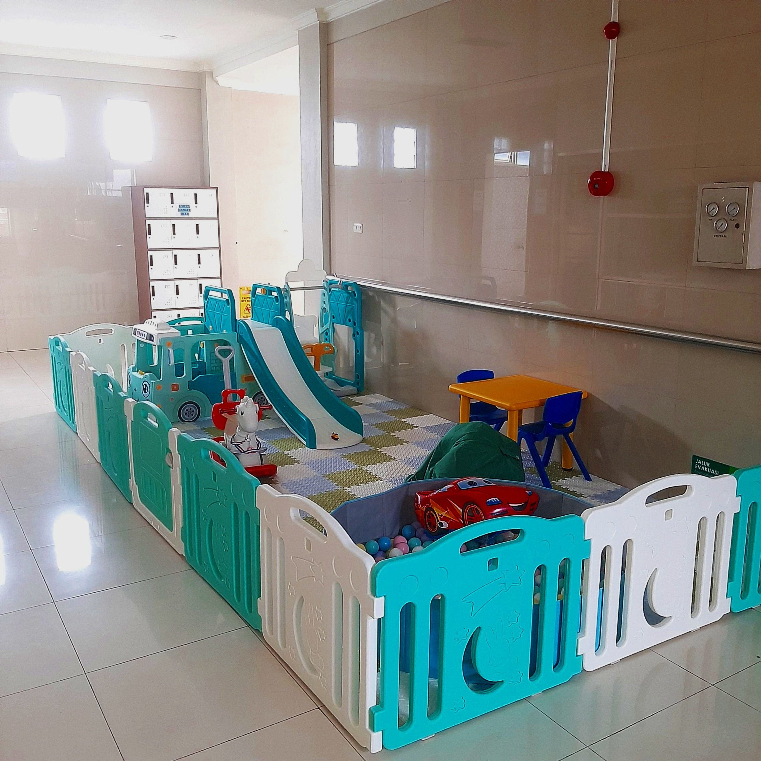 Indoor family play area with a small slide, ball pit, toys, and children’s furniture enclosed by colorful plastic fencing.