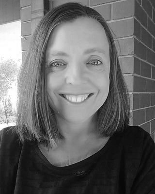 A woman with shoulder-length hair smiling outdoors near a brick wall.