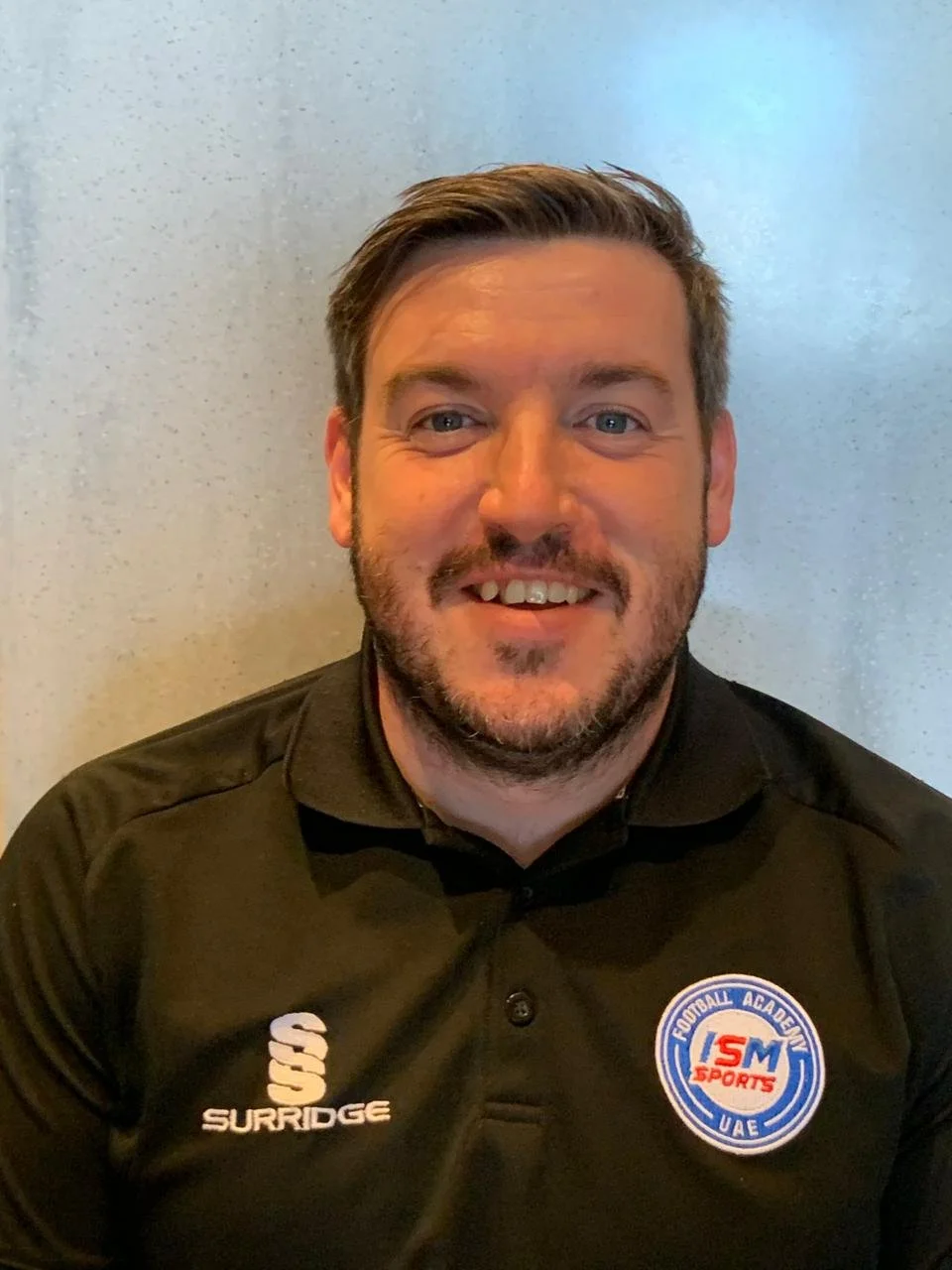 Person in a blue sports shirt holding a red tennis racket, standing on a balcony with a cityscape and waterway view in the background.