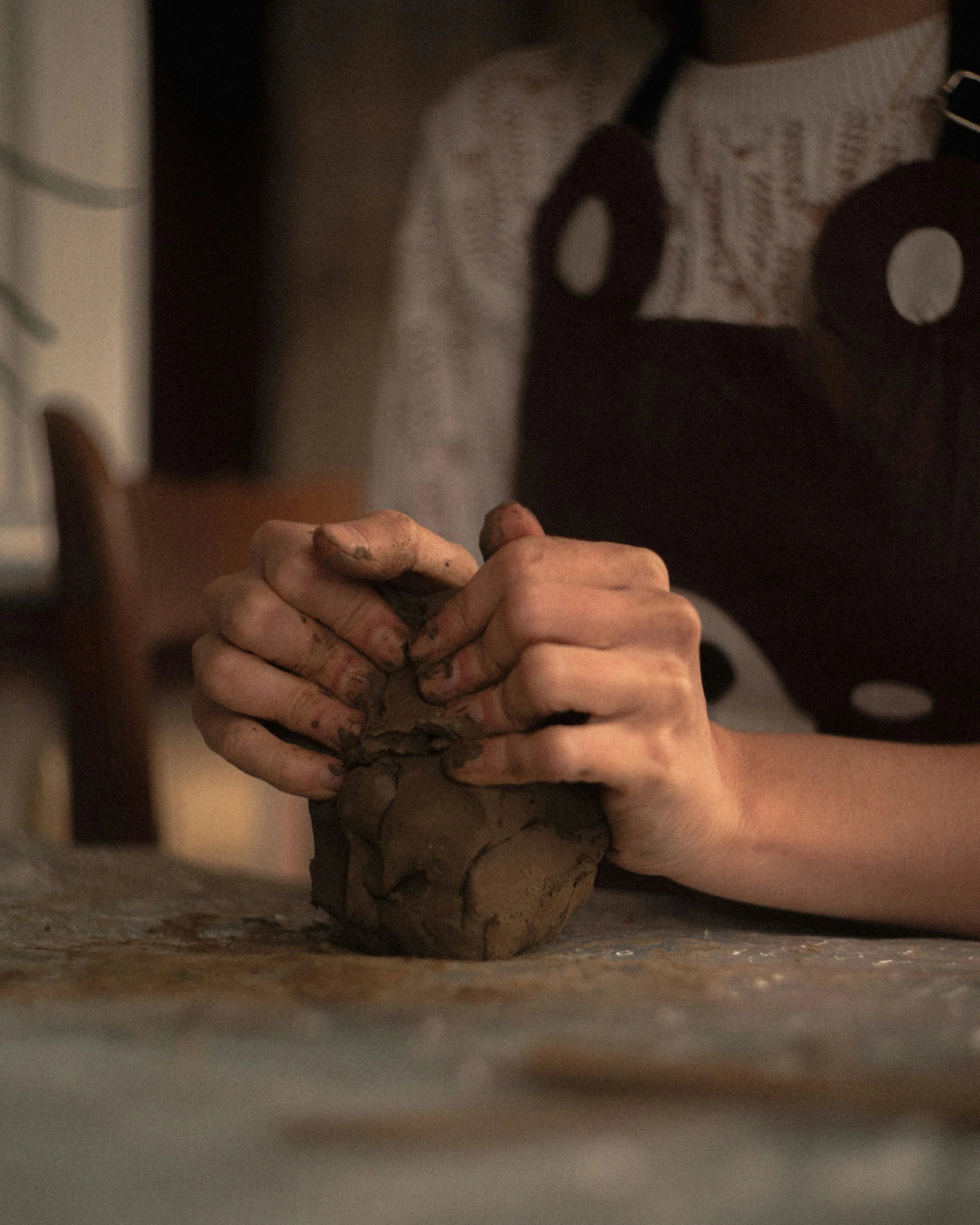 Person's hands kneading brown clay on a table.