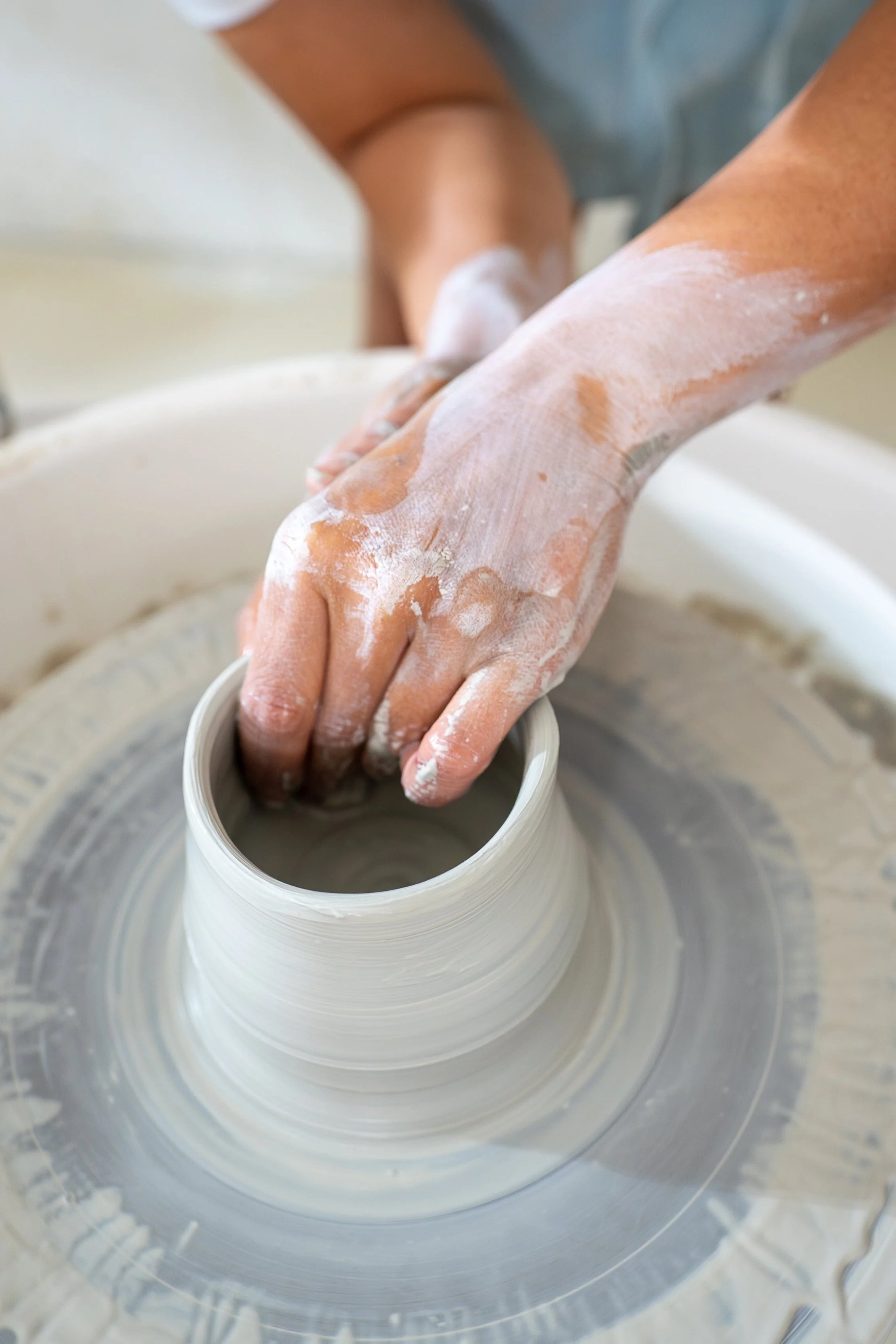 Person shaping clay on a pottery wheel with hands covered in wet clay.