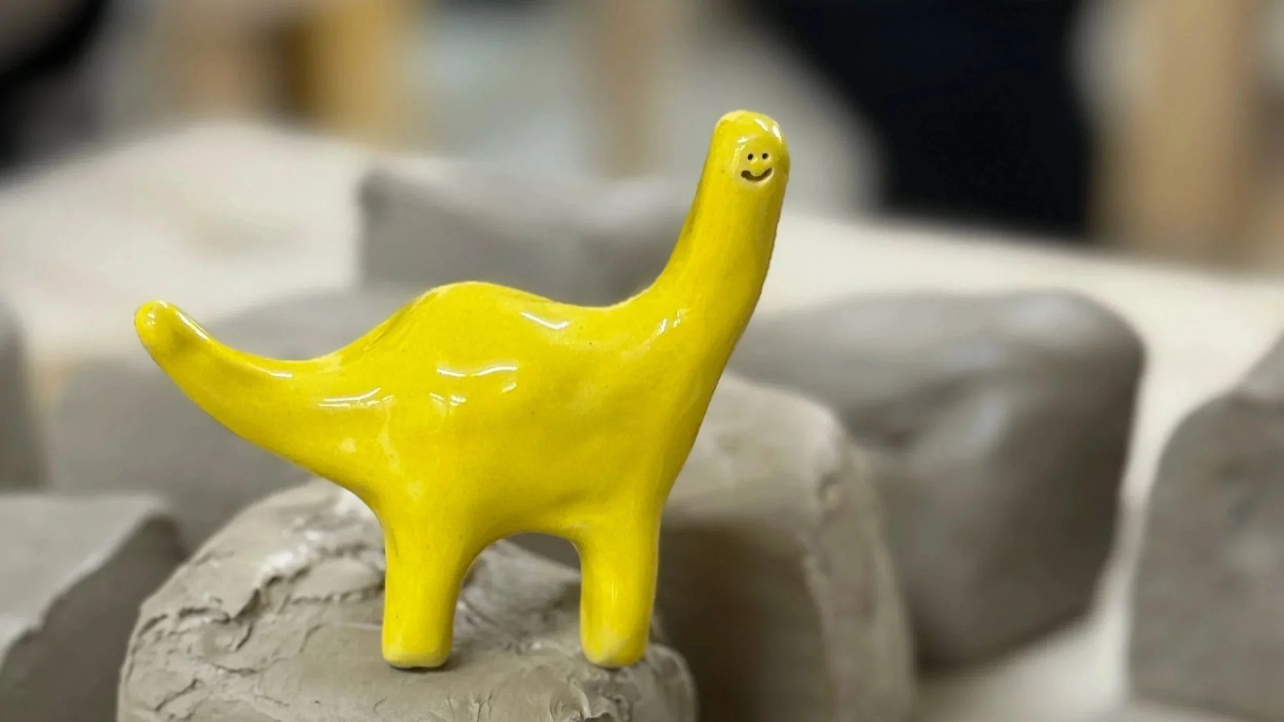 a small yellow ceramic dinosaur stands on top of a pile of clay 