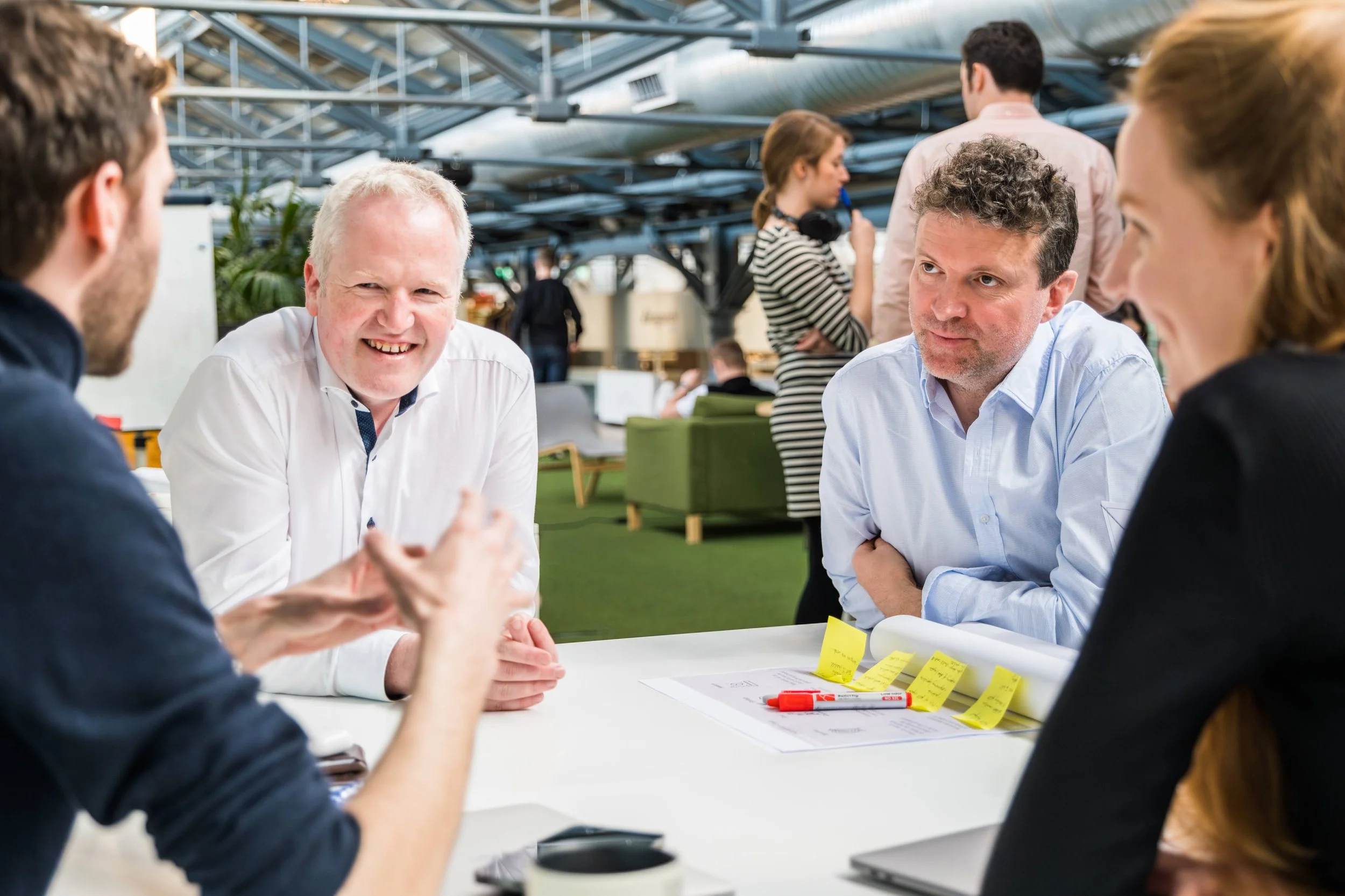 Group of people having a meeting in a modern office setting, with two men and a woman focused on a discussion. Sticky notes and a marker are on the table.