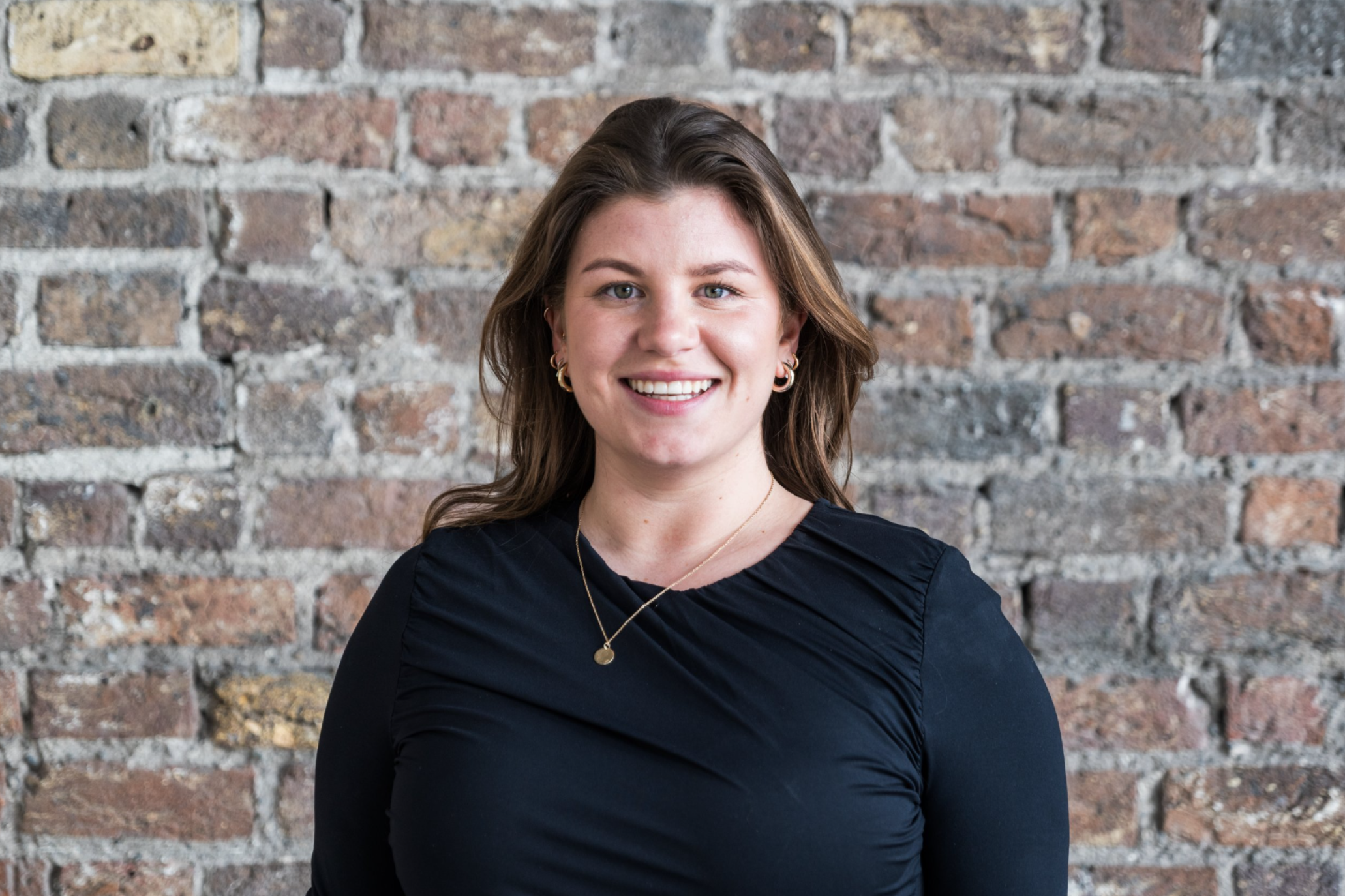 Person smiling in front of a brick wall.