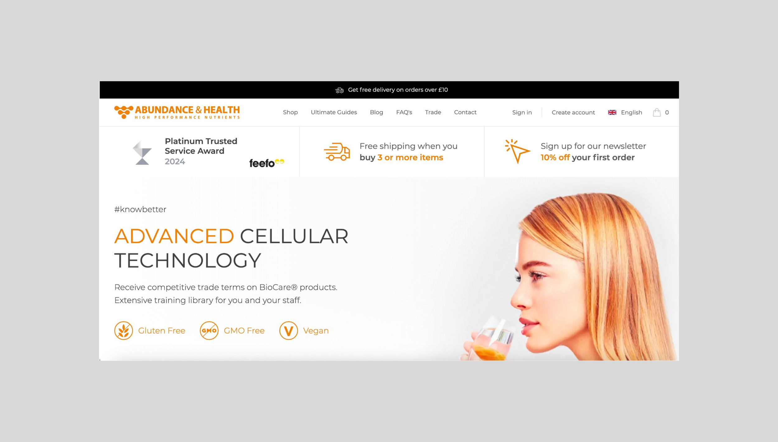 A webpage for Abundance & Health featuring a woman with red hair holding a glass. The page promotes advanced cellular technology, with icons indicating gluten-free, GMO-free, and vegan products. The header includes free delivery, a newsletter sign-up offer, and navigation links.