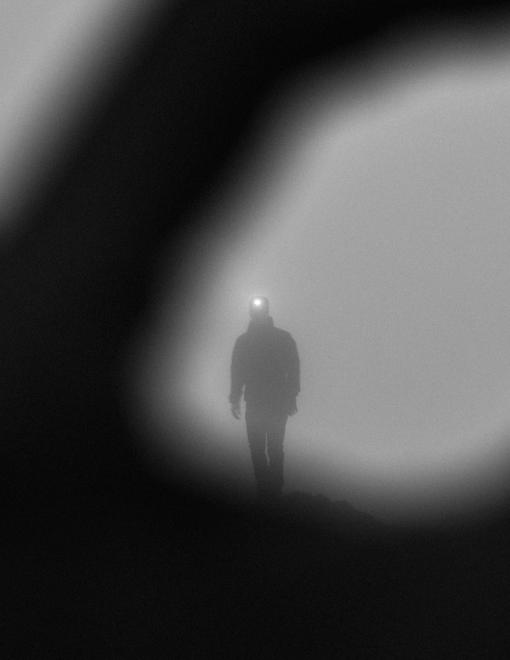 Person walking through fog with headlamp in a dark, misty environment, black and white photo.