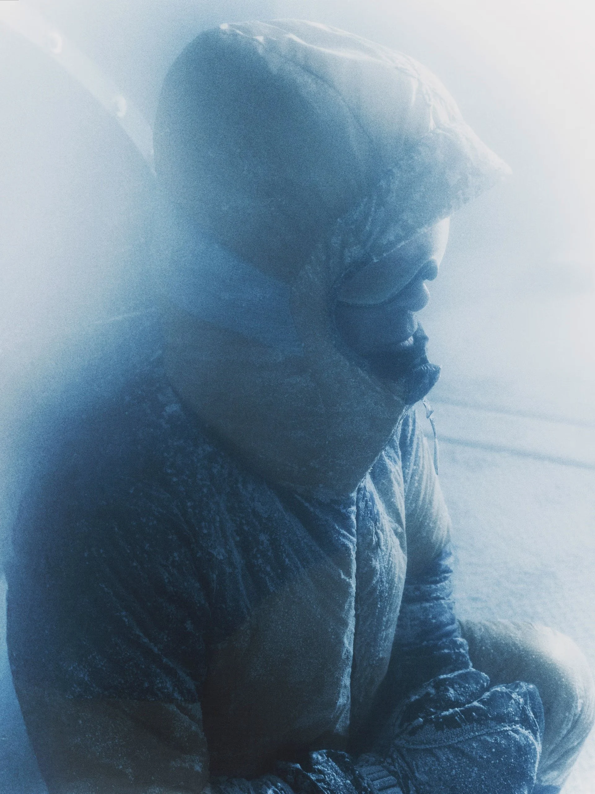 A person with a hooded jacket smiling, in a snowy or icy environment, with snow or ice on their clothing.