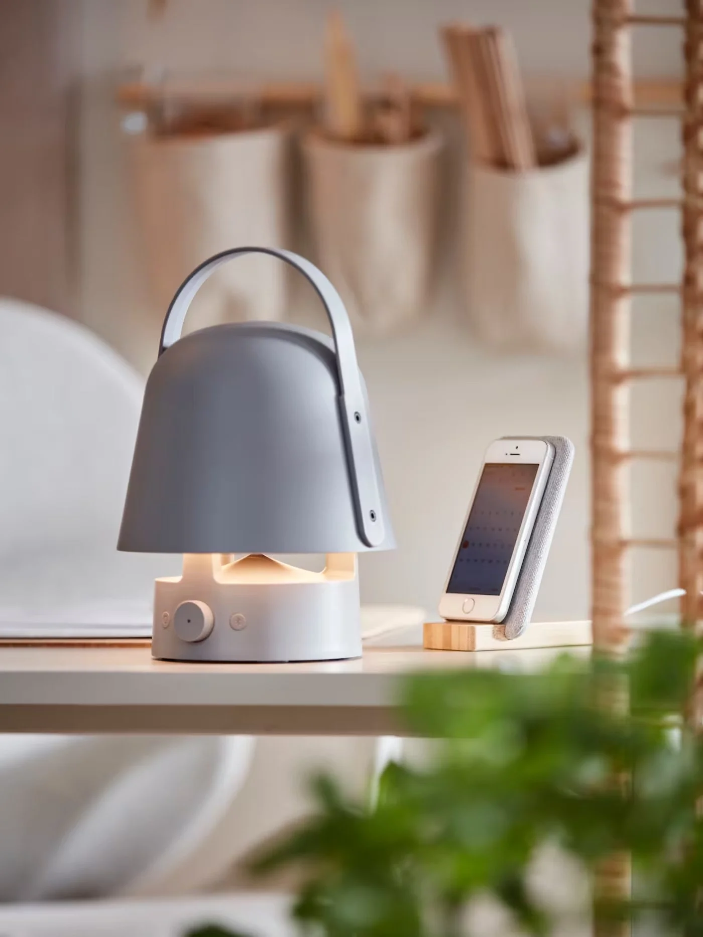 The IKEA portable speaker on a table near a mobile phone in a stand.