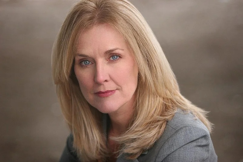 A headshot of Marcy, a white woman with medium blonde hair and blue eyes.