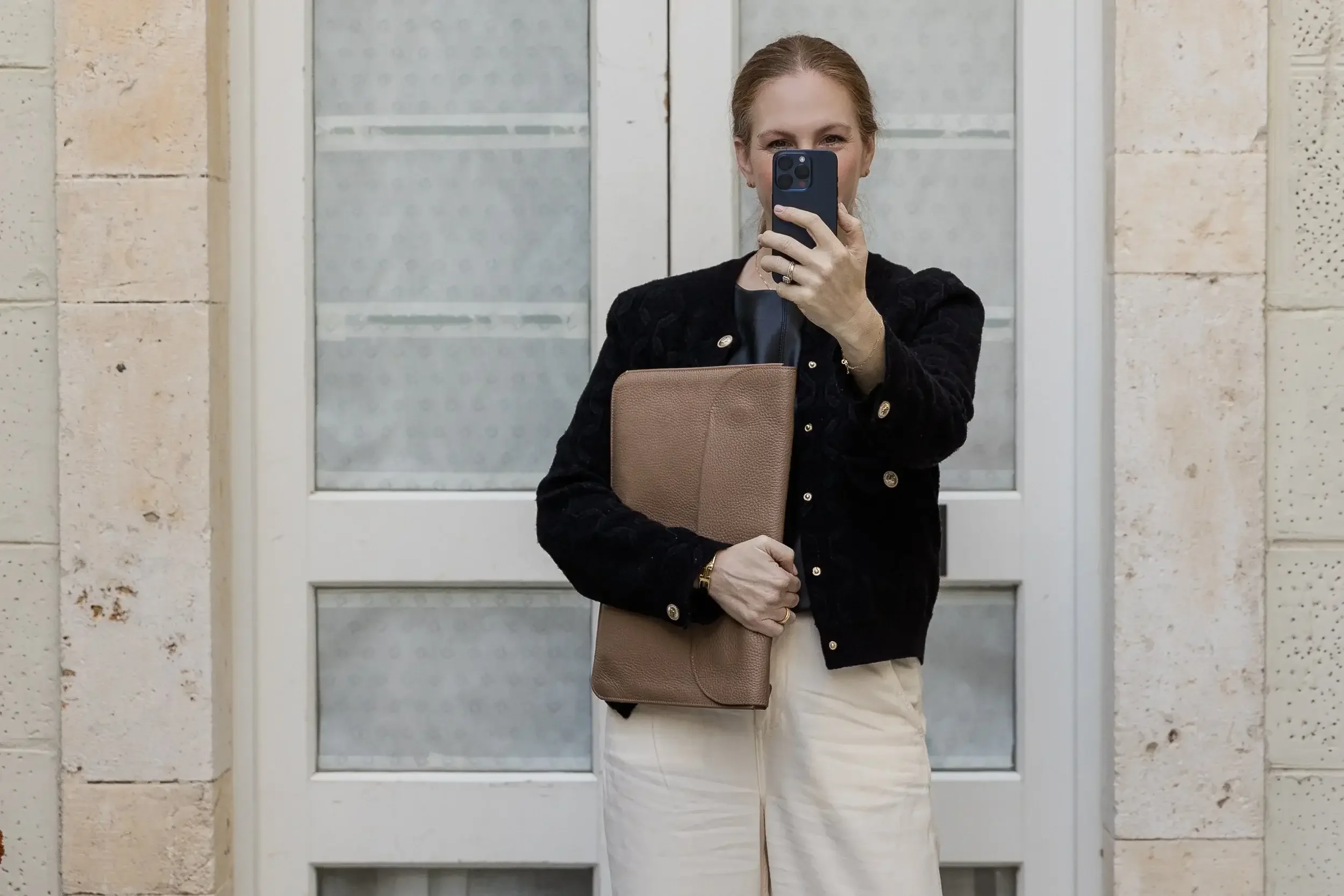 Karen Hamou, MBA admissions consultant, taking a mirror selfie in a black jacket and beige trousers