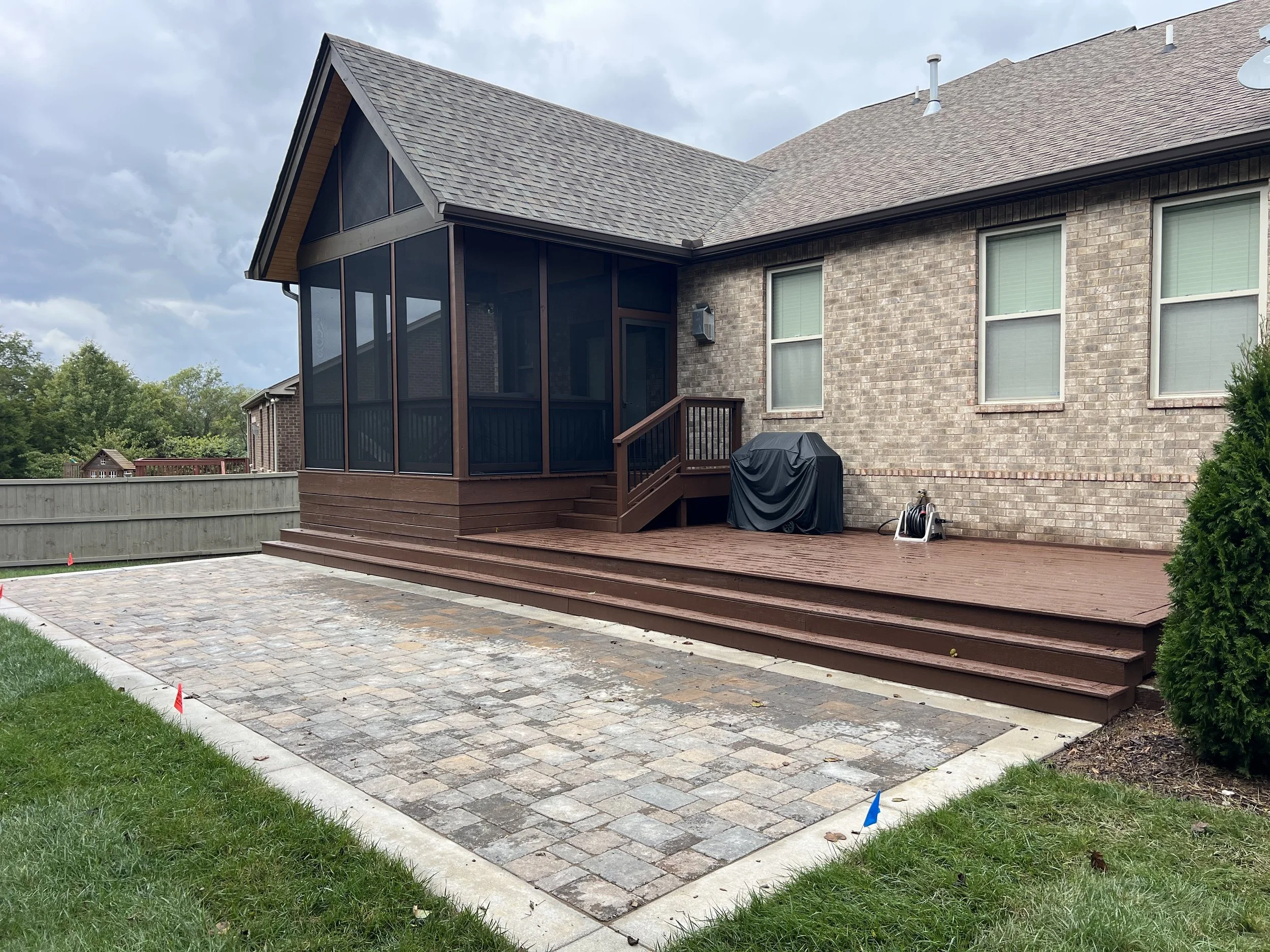 Backyard with a brick house, screened-in porch, wooden deck, and newly paved area.
