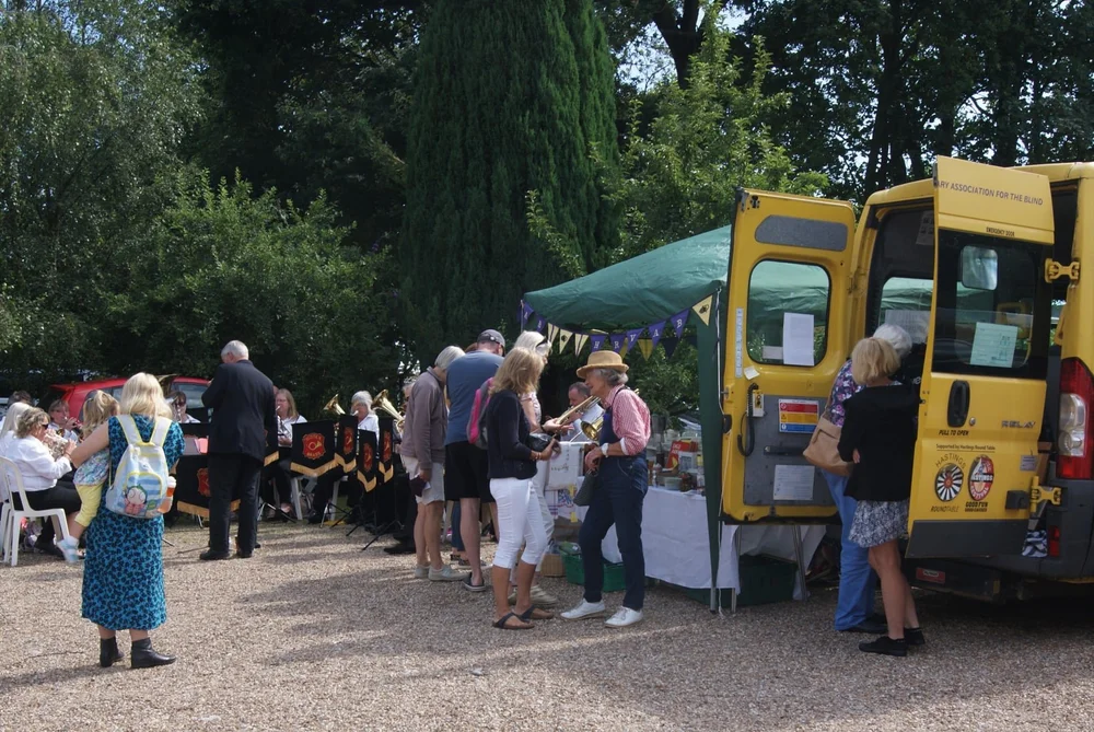 Visitors, a brass band and the yellow HRVAB minibus at an outdoor fundraising day