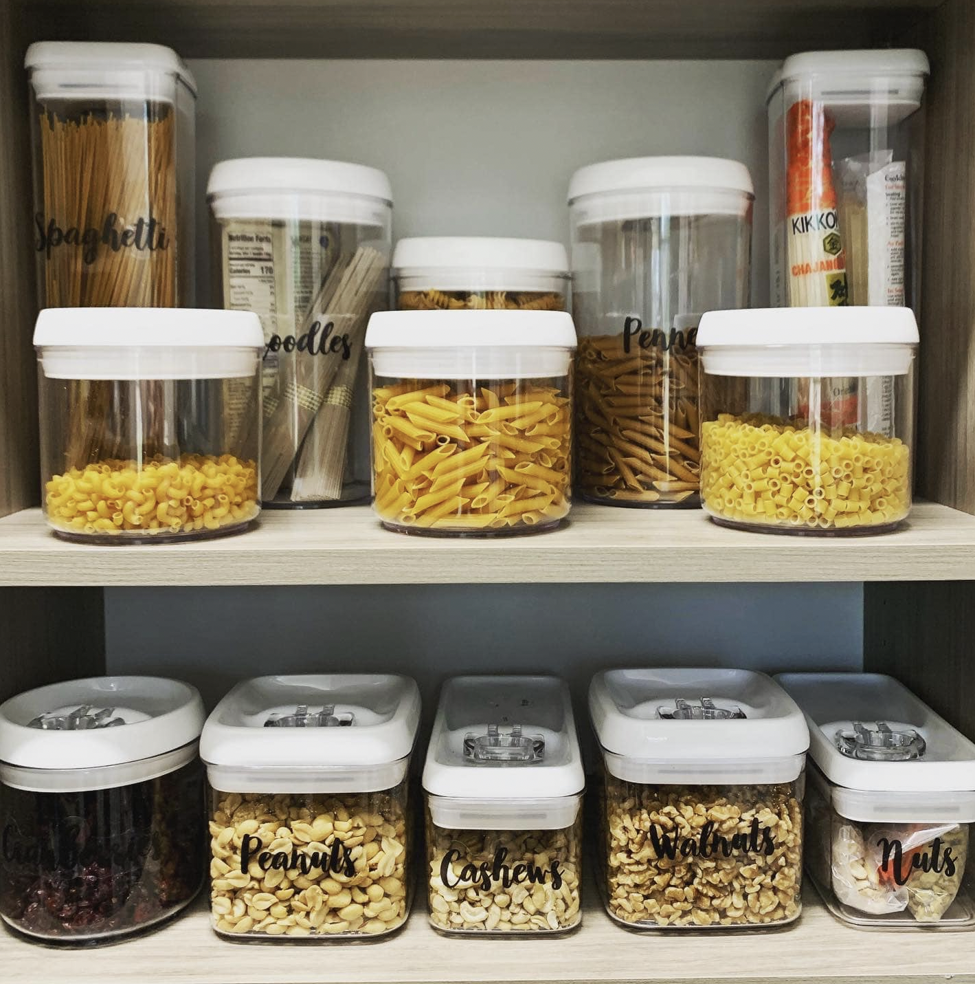 Organized kitchen pantry in Atlanta,  with labeled clear containers holding different types of pasta, nuts, and dried fruits.