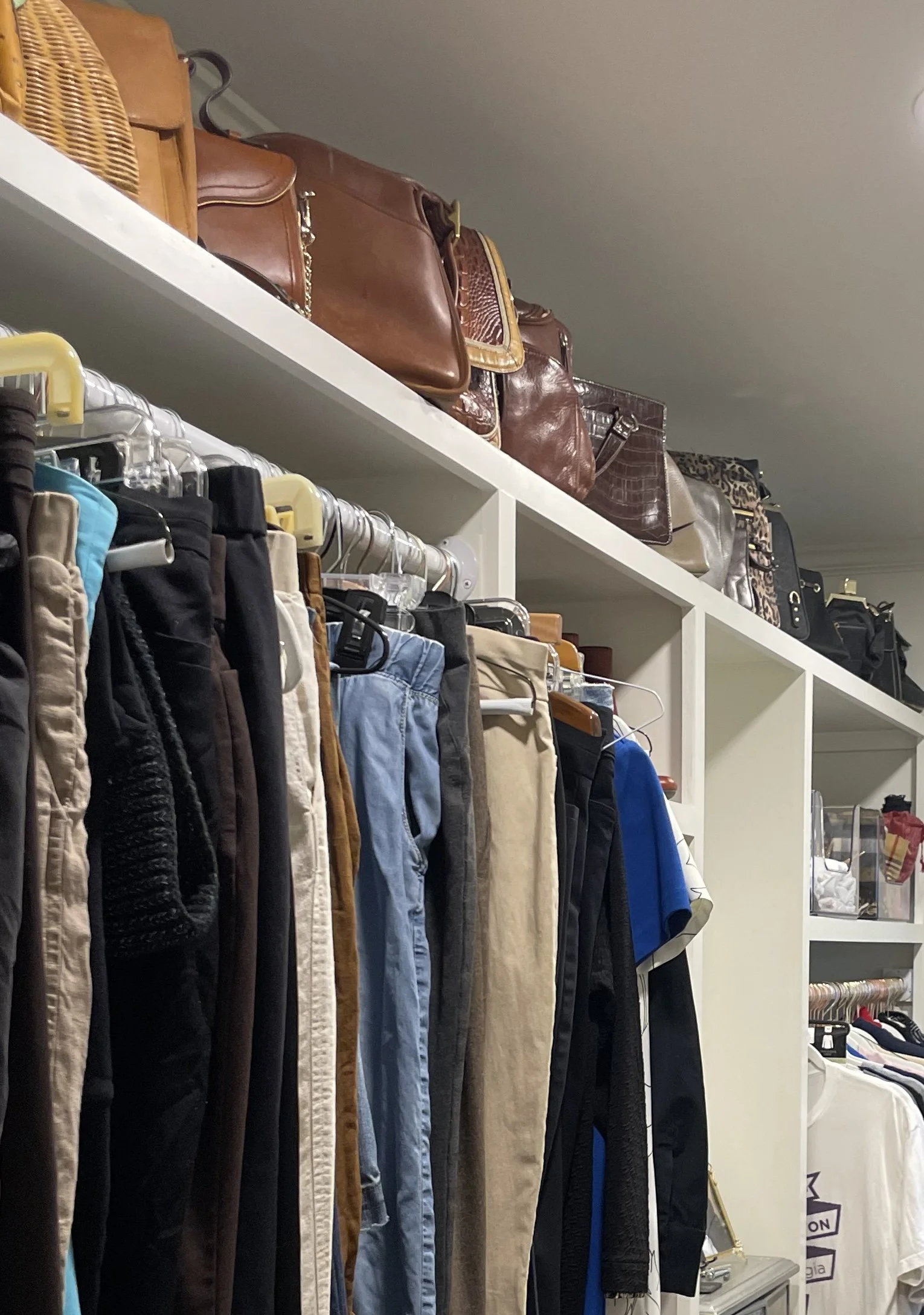 An organized Decatur closet with a collection of pants hanging on a rack. Luxury handbags are sorted and organized in the closet.