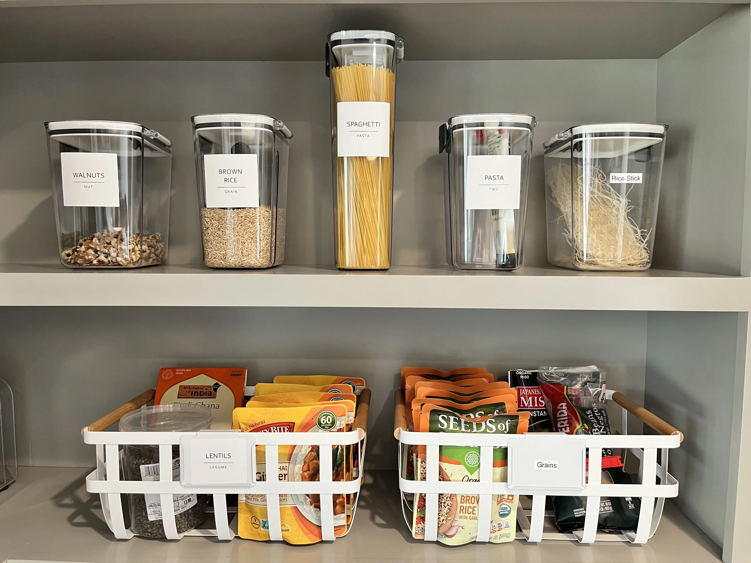 Organized kitchen pantry shelf in Decatur, GA. Shows organized and labeled clear containers. Below are eco-friendly organizing baskets. Sustainable and thoughtful organizing is a focus for Happy Tree Organizing. 