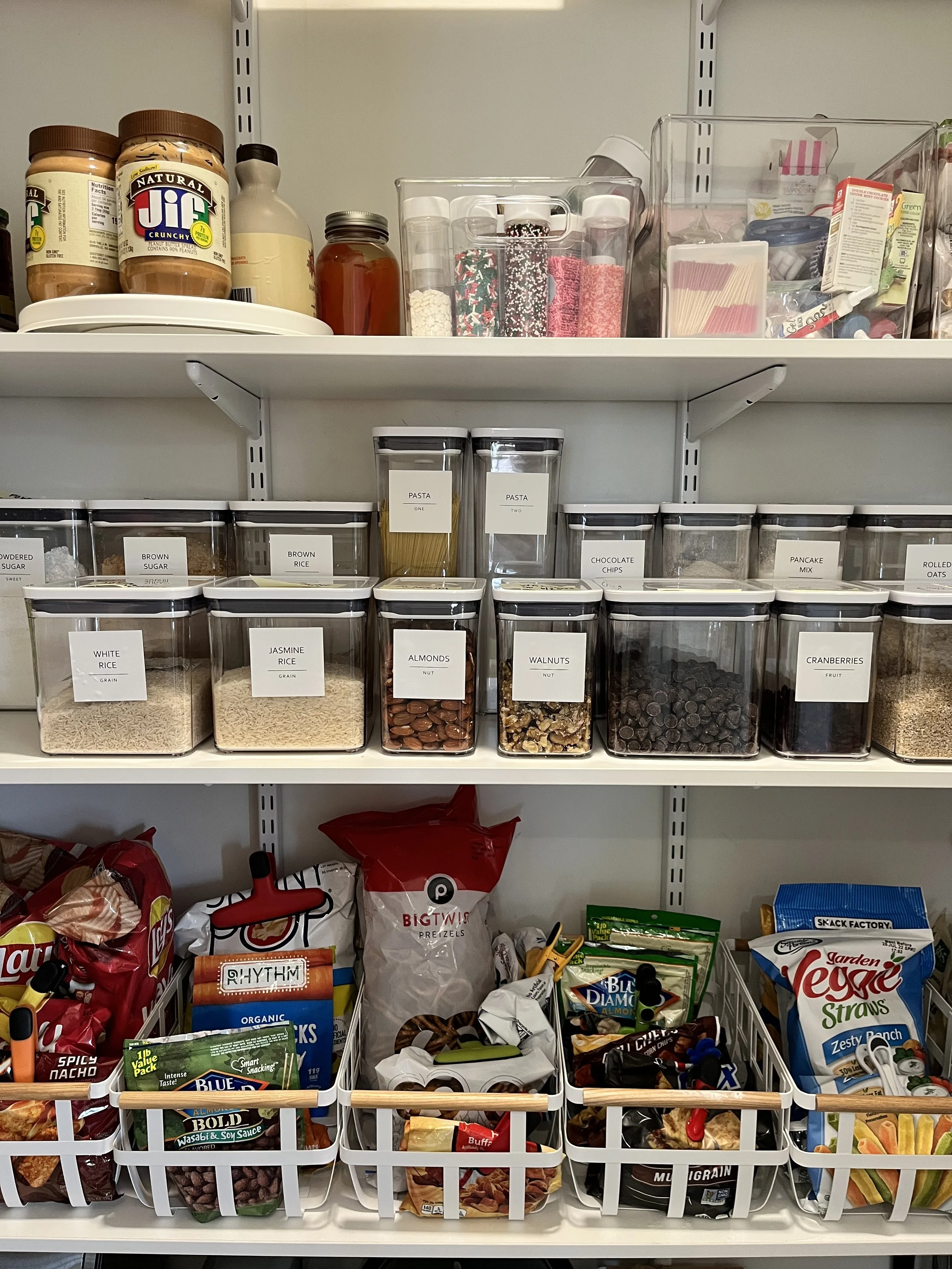 Decluttered pantry shelves with organized jars of baking ingredients, snack bags, and food storage containers. 