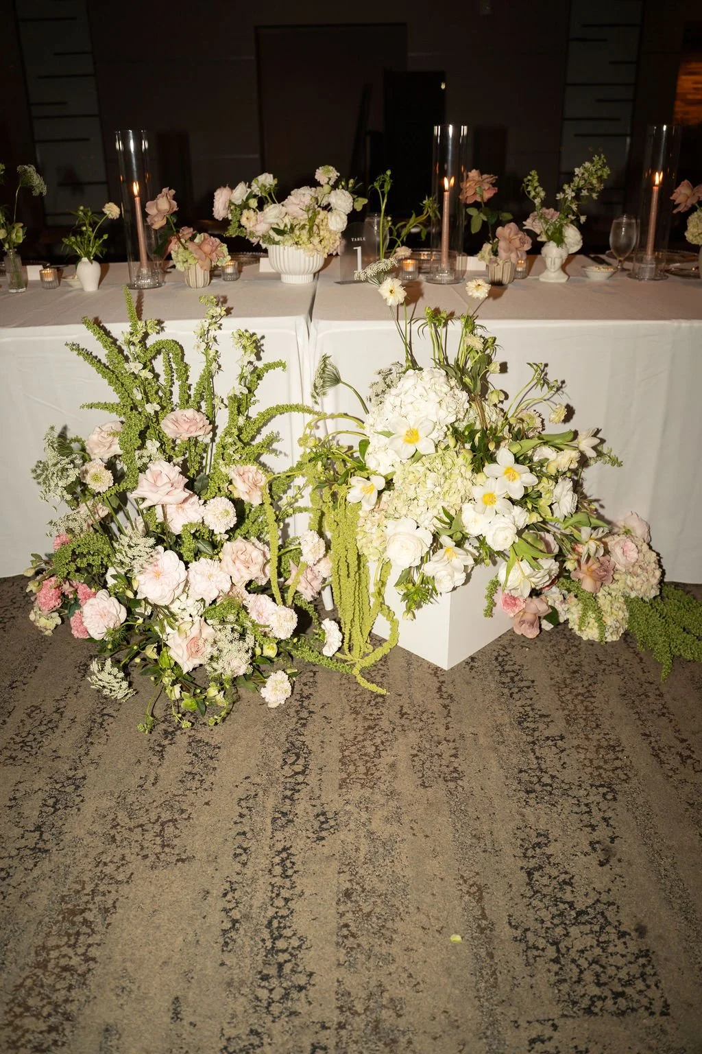 Elegant table decorated with white and blush pink floral arrangements, candles, and tall glass vases.
