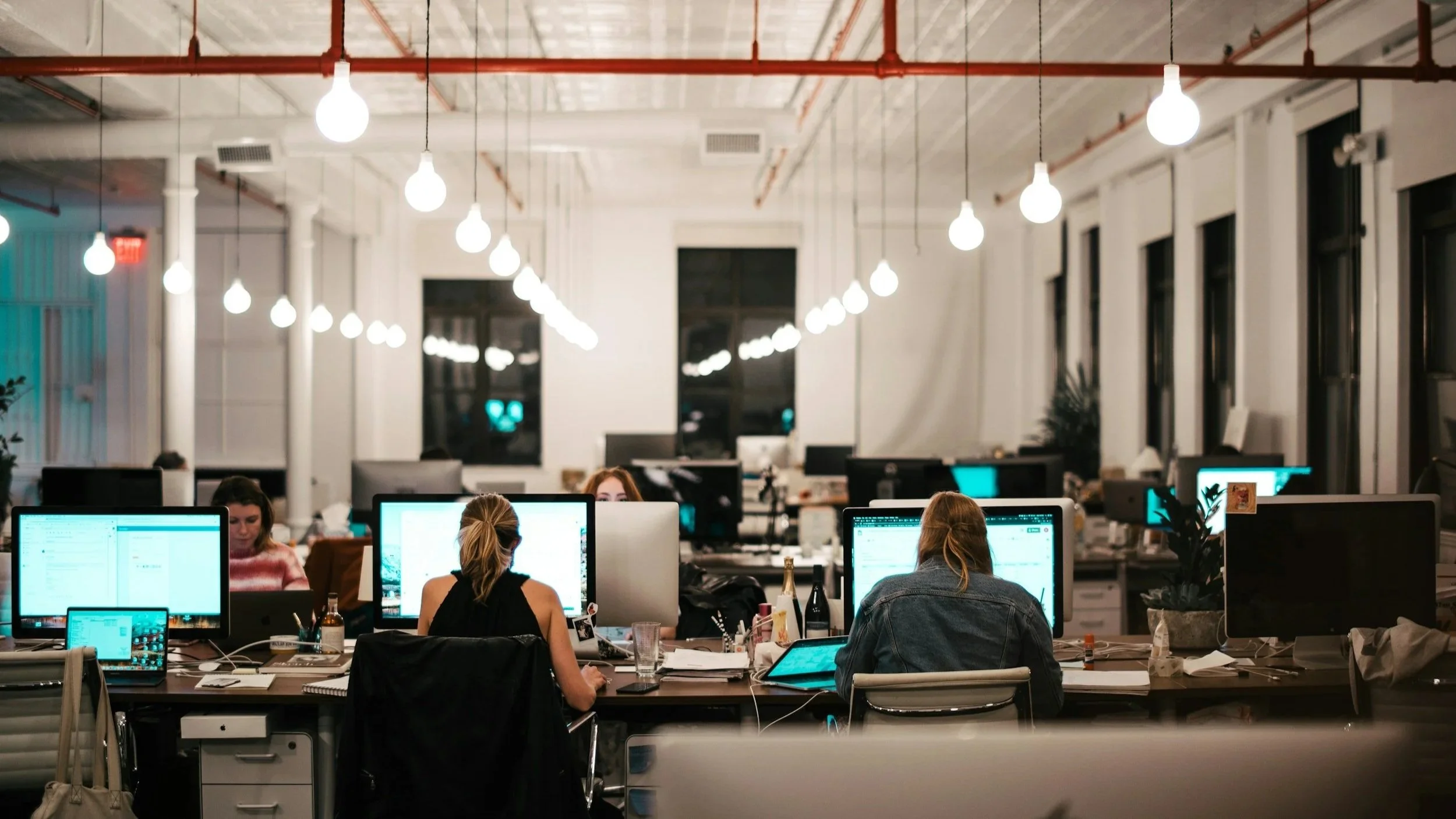 Vue d'un bureau open space moderne et lumineux. Plusieurs collaborateurs sont installés à leurs postes de travail, concentrés sur leurs écrans d'ordinateur. Ambiance de travail professionnelle et collaborative.