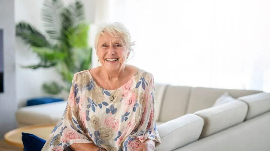 Senior woman smiling comfortably in her home, representing compassionate downsizing support during a life transition.