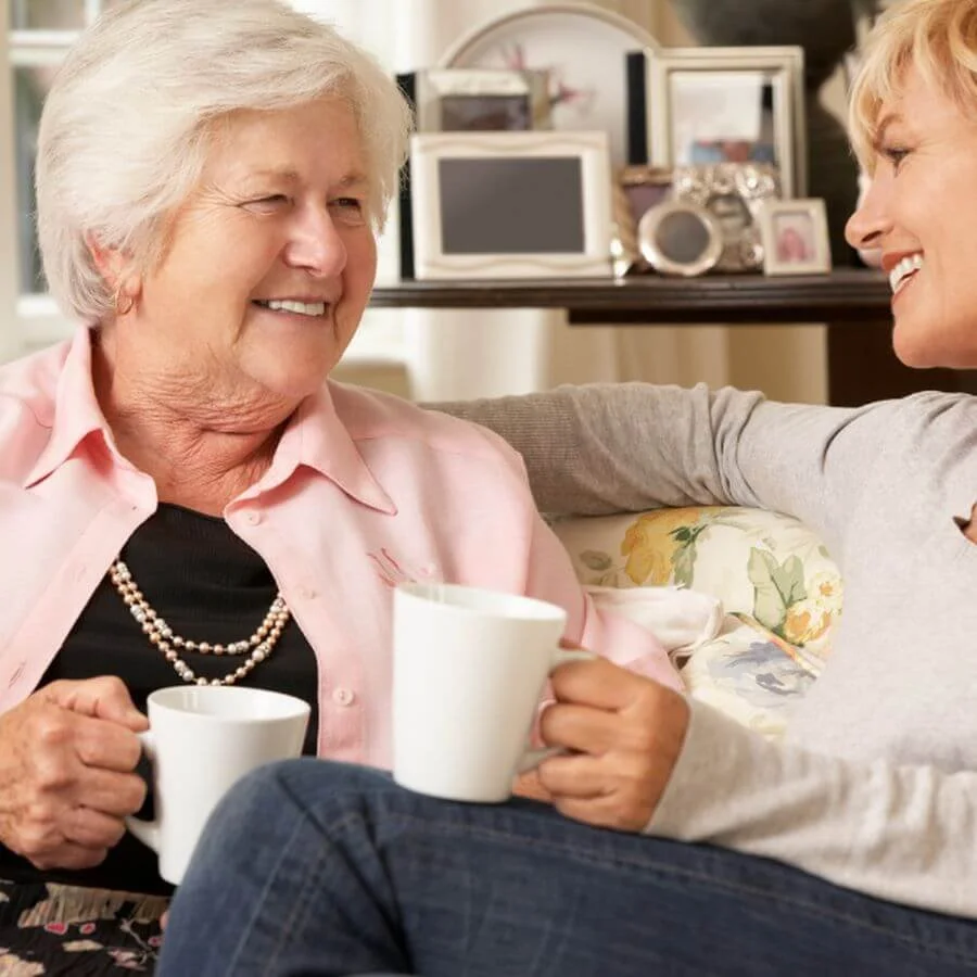 Older woman and her adult daughter smiling together at home, representing compassionate support while navigating a downsizing transition.