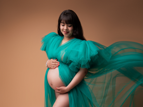 Embarazada con vestido de tul azul oscuro, posando con sonrisa y manos en su barriga.
