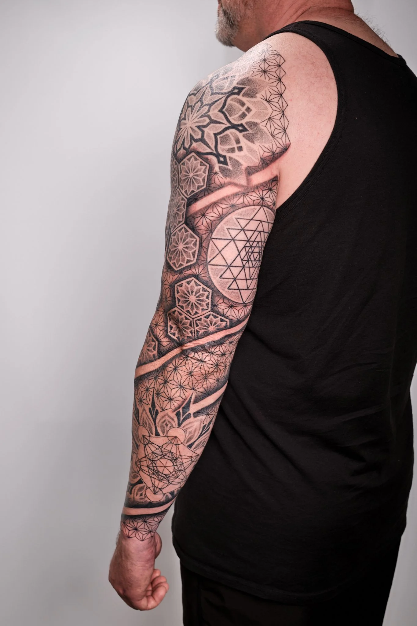 Geometric tattoo sleeve with asanoha and hexagonal mandalas, sacred symbols, and Norse mythology elements in blackwork style.