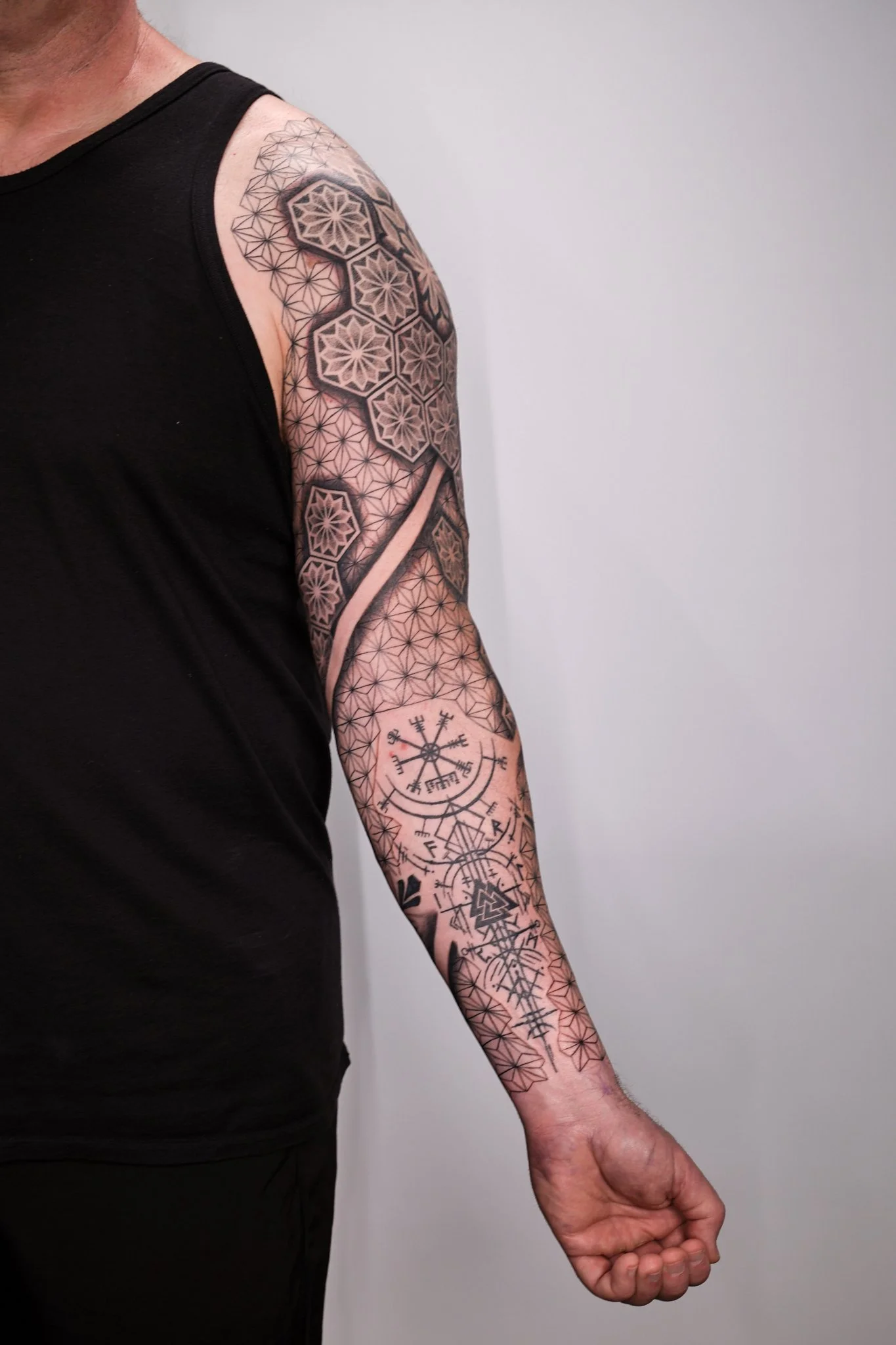 Sleeve tattoo with sacred geometry, negative space ribbon, and Norse protection symbols like Vegvisir and Valknut