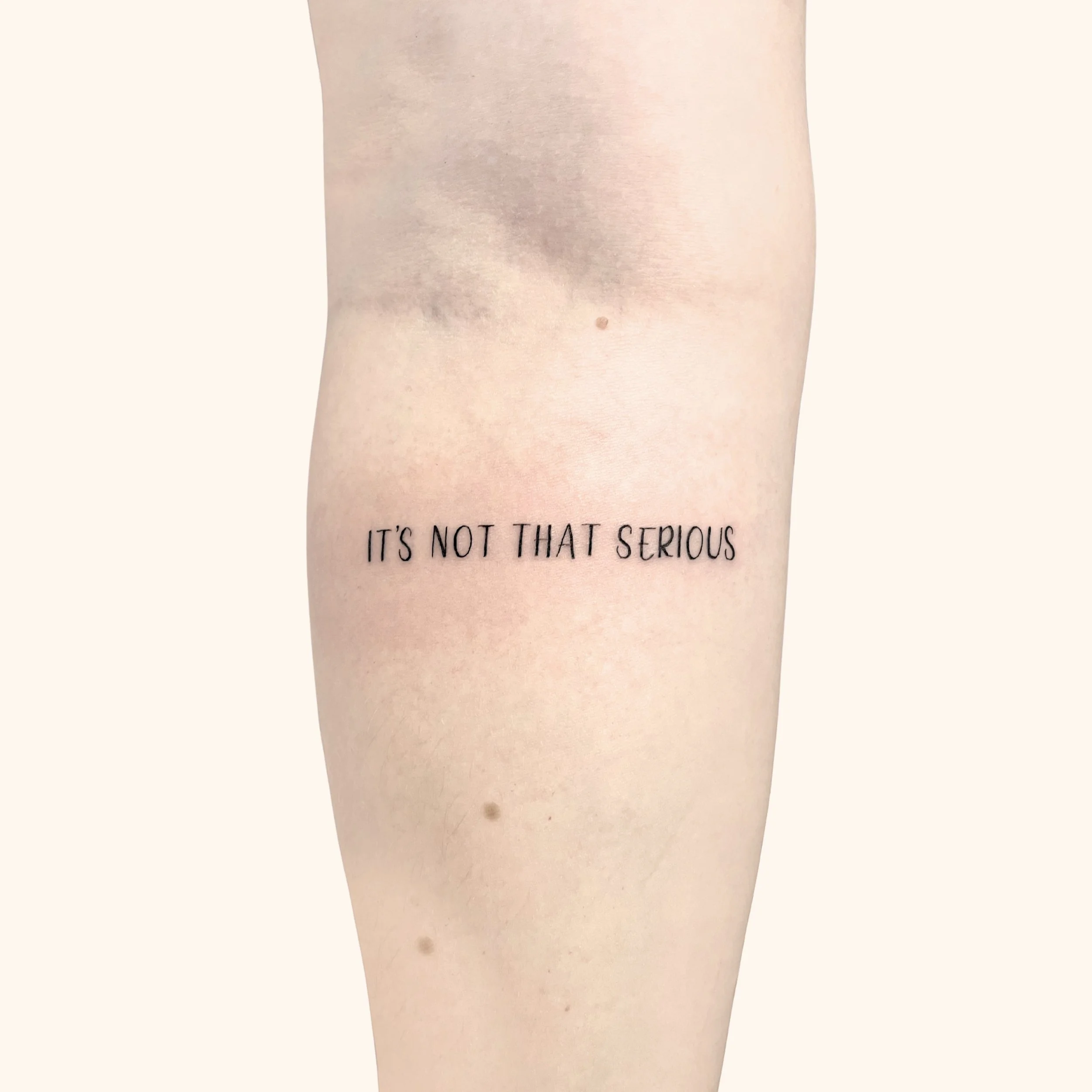 "It's not that serious" print script tattoo on a forearm in capital letters