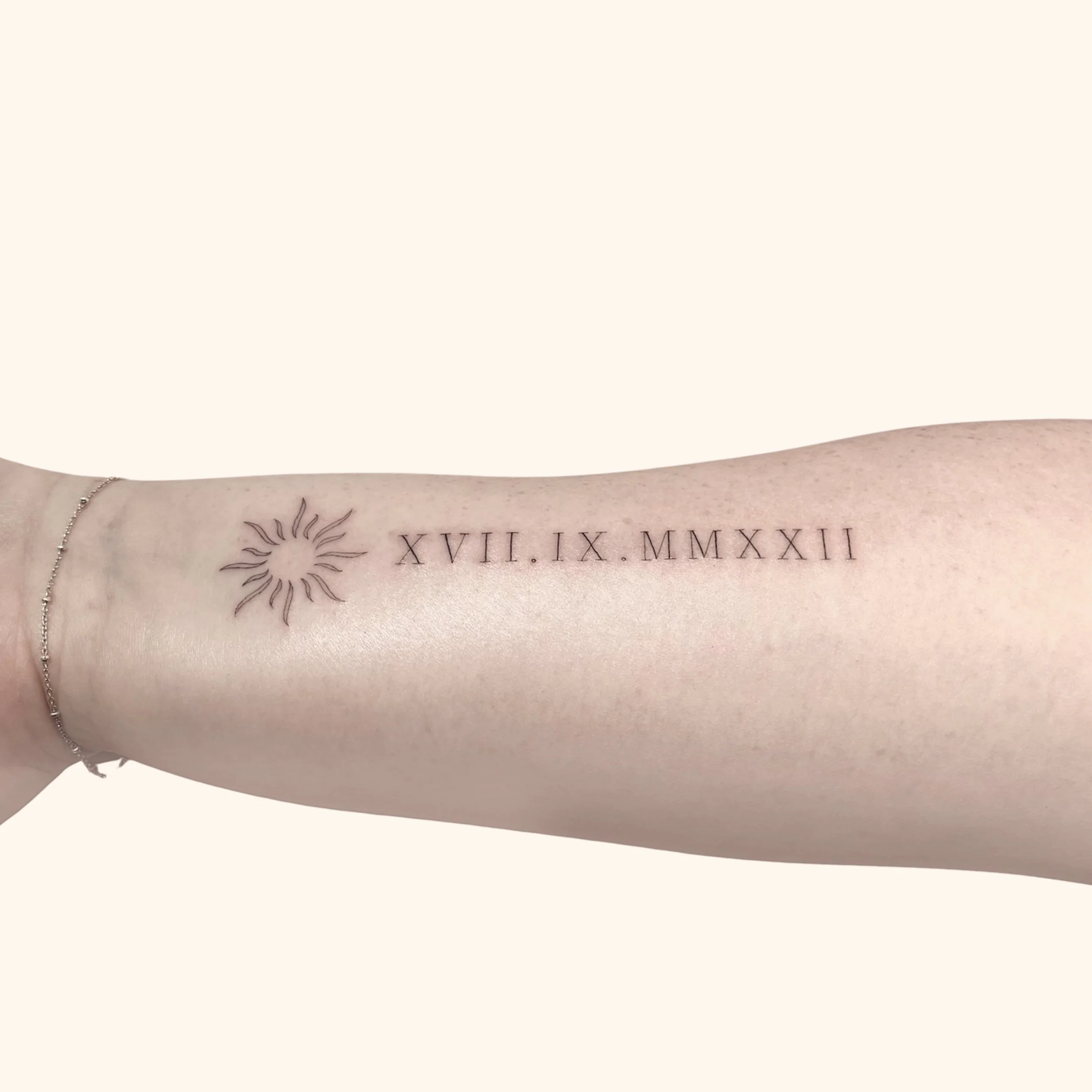 "XVII IX MMXXII" Roman Numerals 17 - 9 - 2022 tattoo in captial letters with a small sun tattoo preceeding it. Inked in Victora BC by Fine Line Laurie