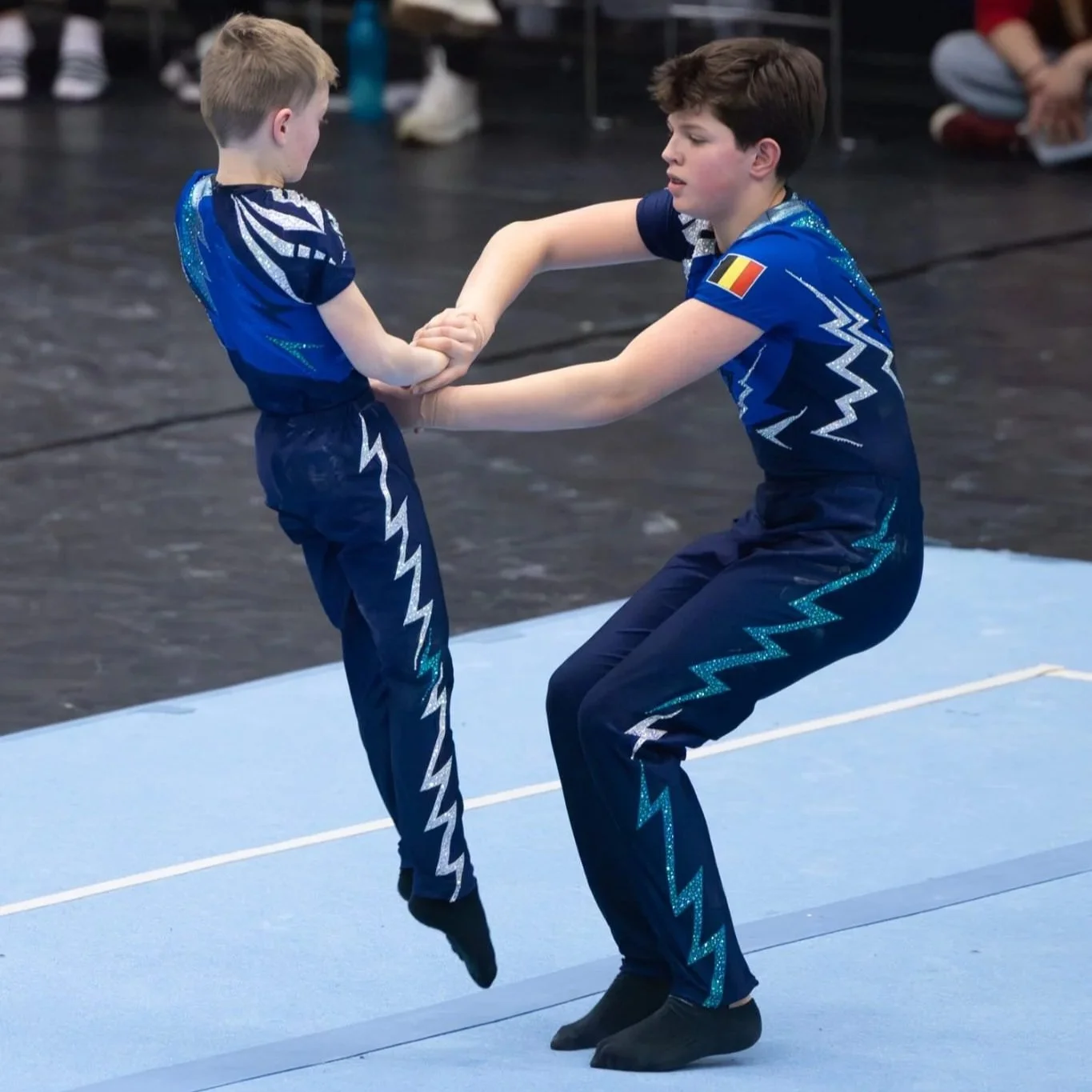 Twee jongens in blauwe unitard van Atelier Nadja & Tutti Leotards oefenen samen op een gymnastiekmat.