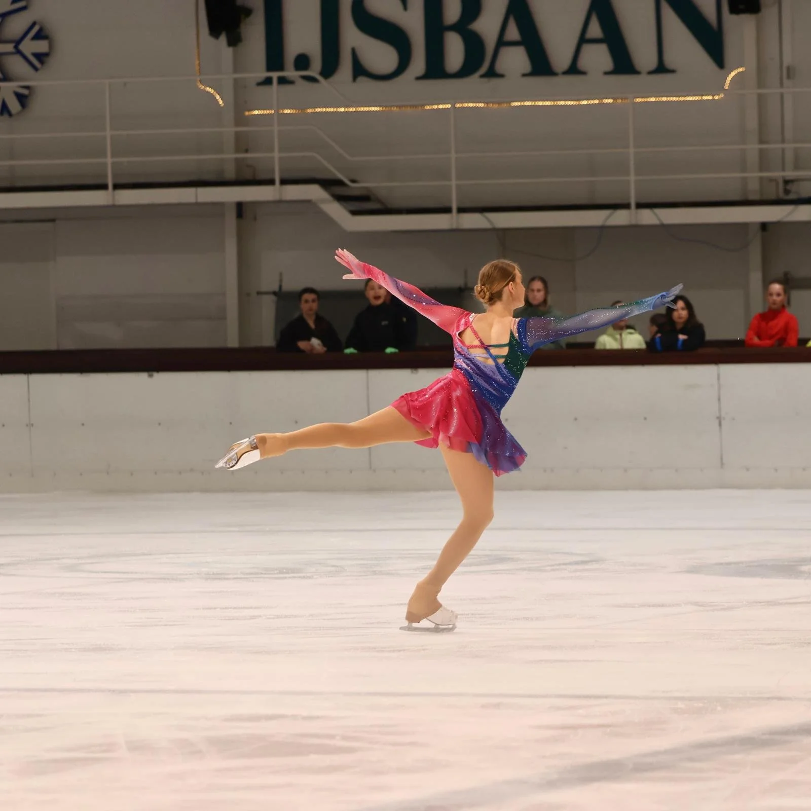 Schaatster in evenwichtselement met roze en blauw pakje van Atelier Nadja & Tutti Leotards