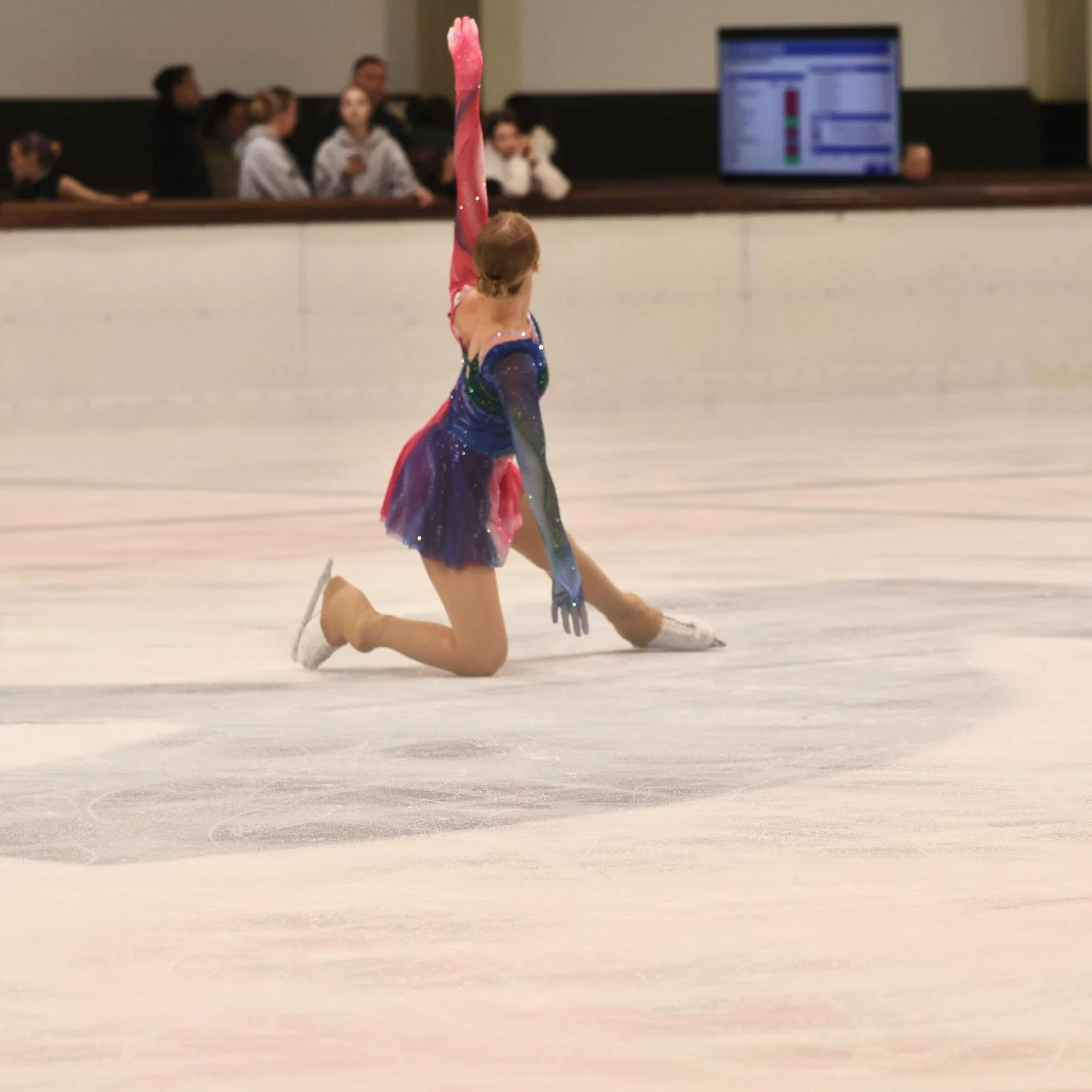 Schaatster met kleurrijk pakje op maat van Atelier Nadja & Tutti Leotards in dansbeweging.