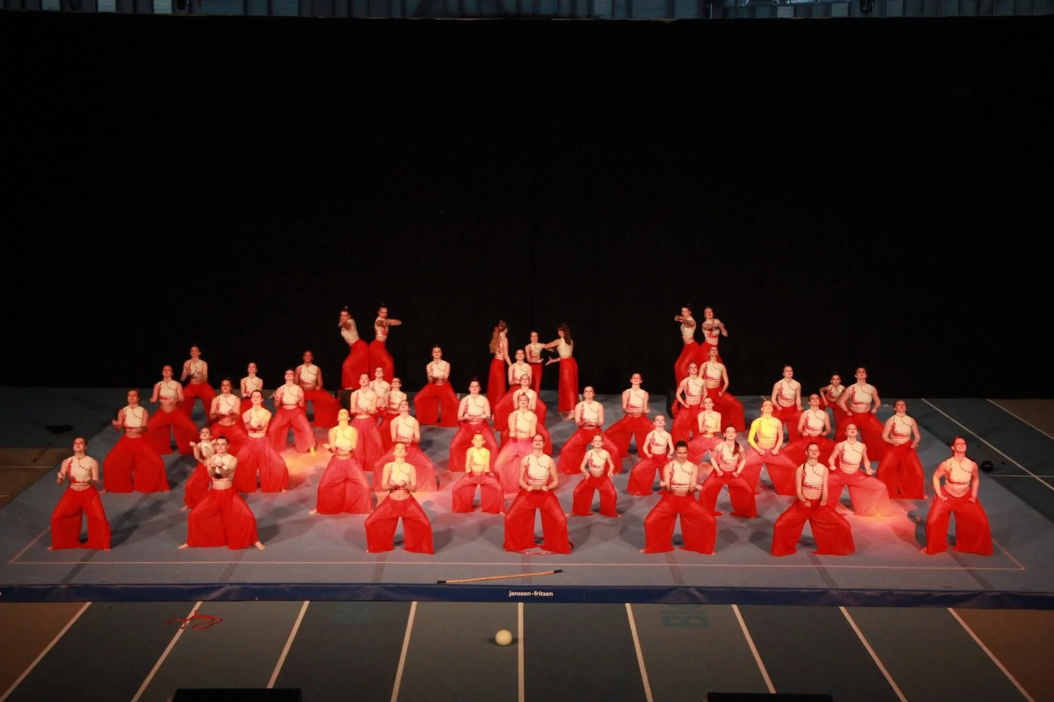Groep mensen in kleurrijke kleding die een dansvoorstelling uitvoeren op een podium met een zwarte achtergrond.