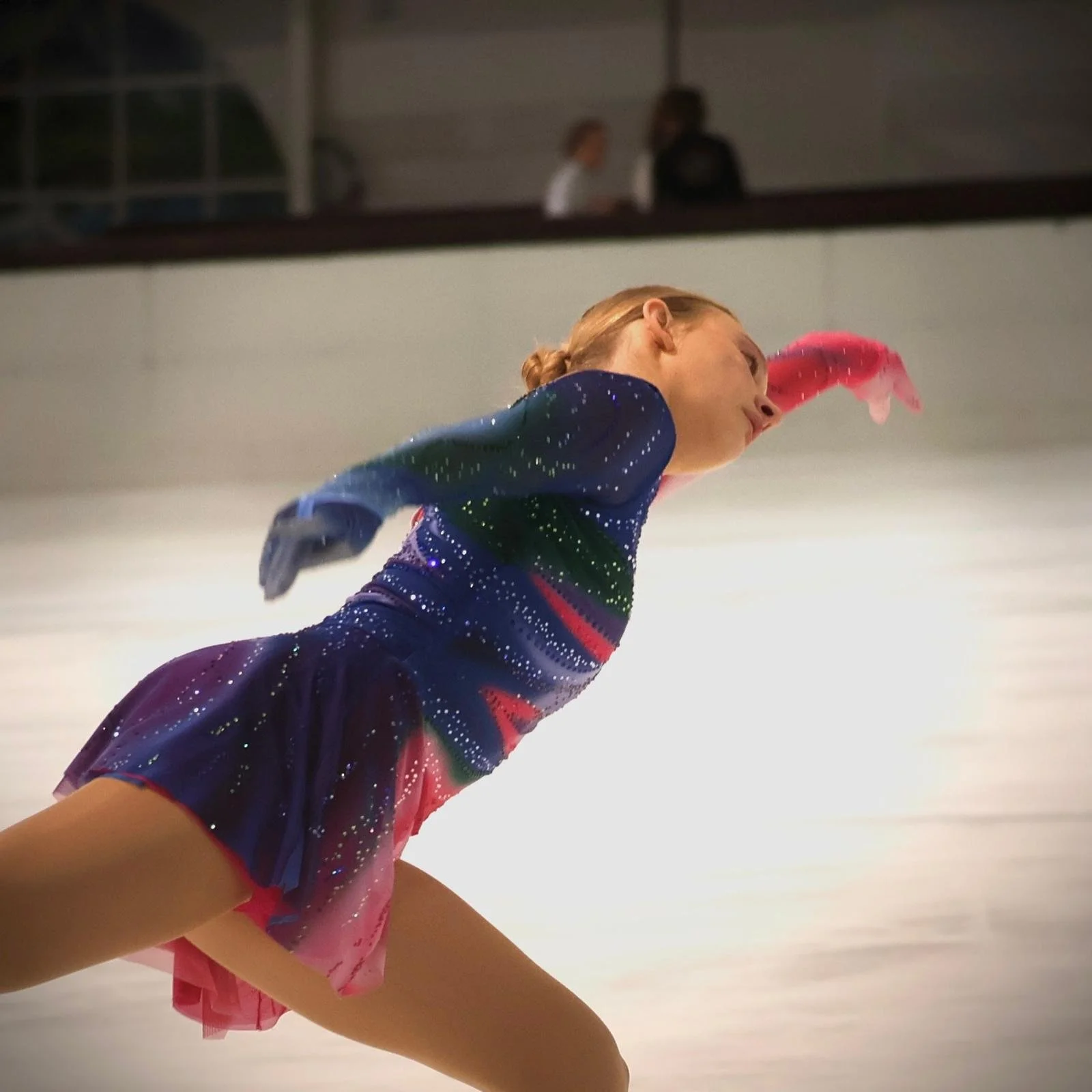 Schaatster in danspose op wedstrijd met pakje in blauw, groen en rozetinten van Atelier Nadja & Tutti Leotards