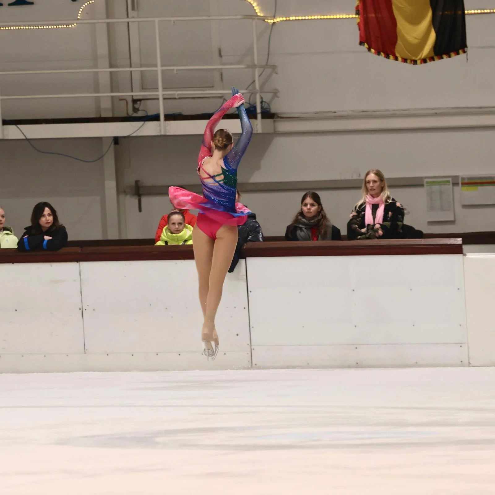 Schaatster tijdens sprong met kleurrijk pakje in blauw en roze tinten van Atelier Nadja & Tutti Leotards