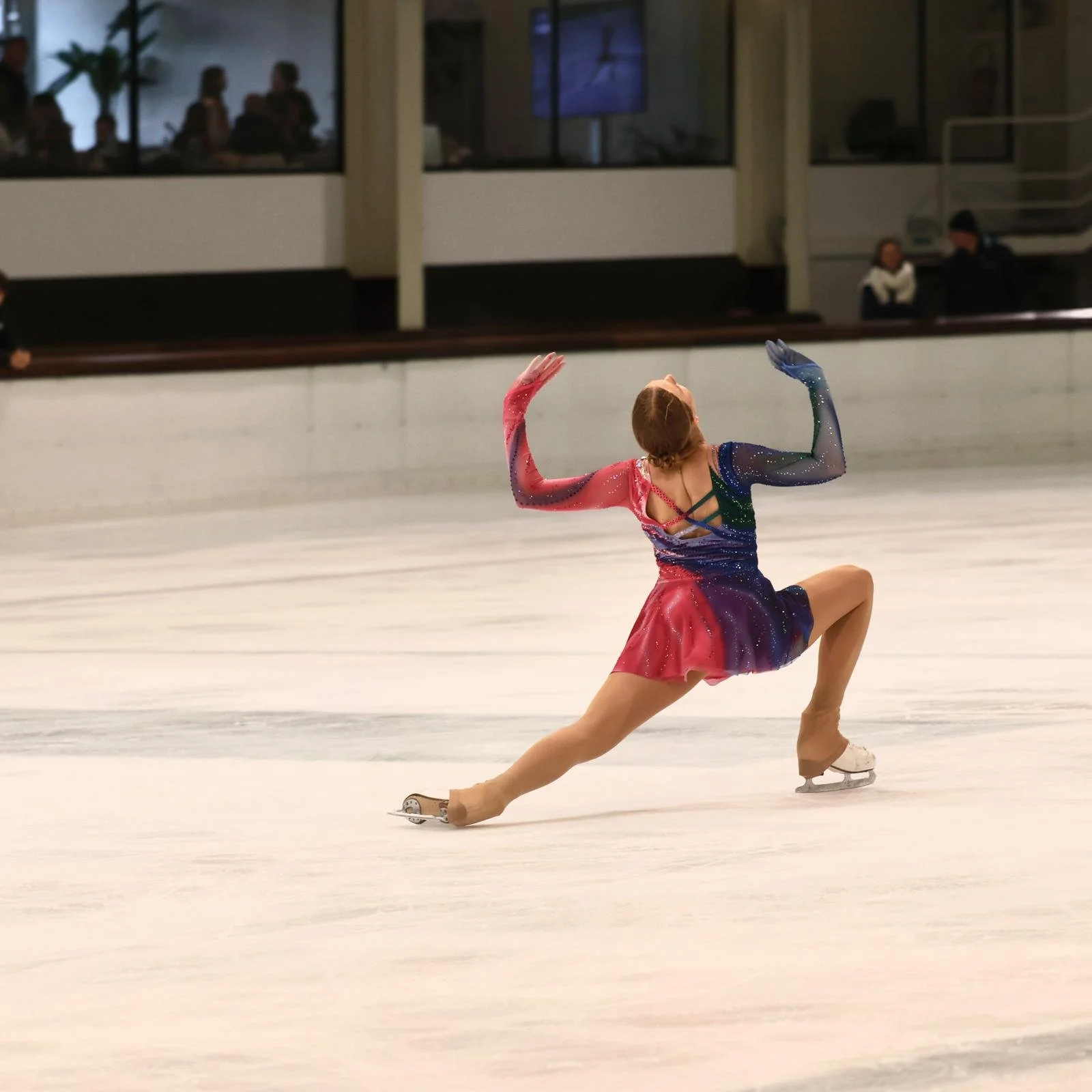 Schaatster tijdens uitvoeren van reeks met kleurrijk pakje in roze en blauwtinten van Atelier Nadja & Tutti Leotards