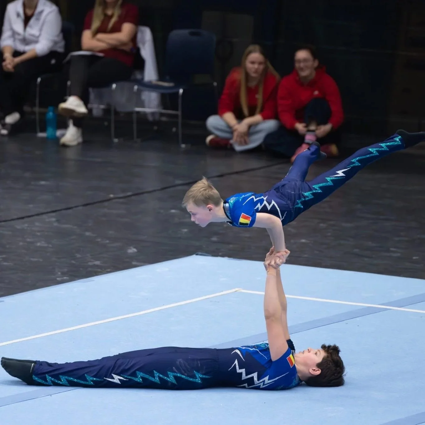 Twee jonge gymnasten voeren een plank uit in een unitard met blauwtinten van Atelier Nadja & Tutti Leotards.