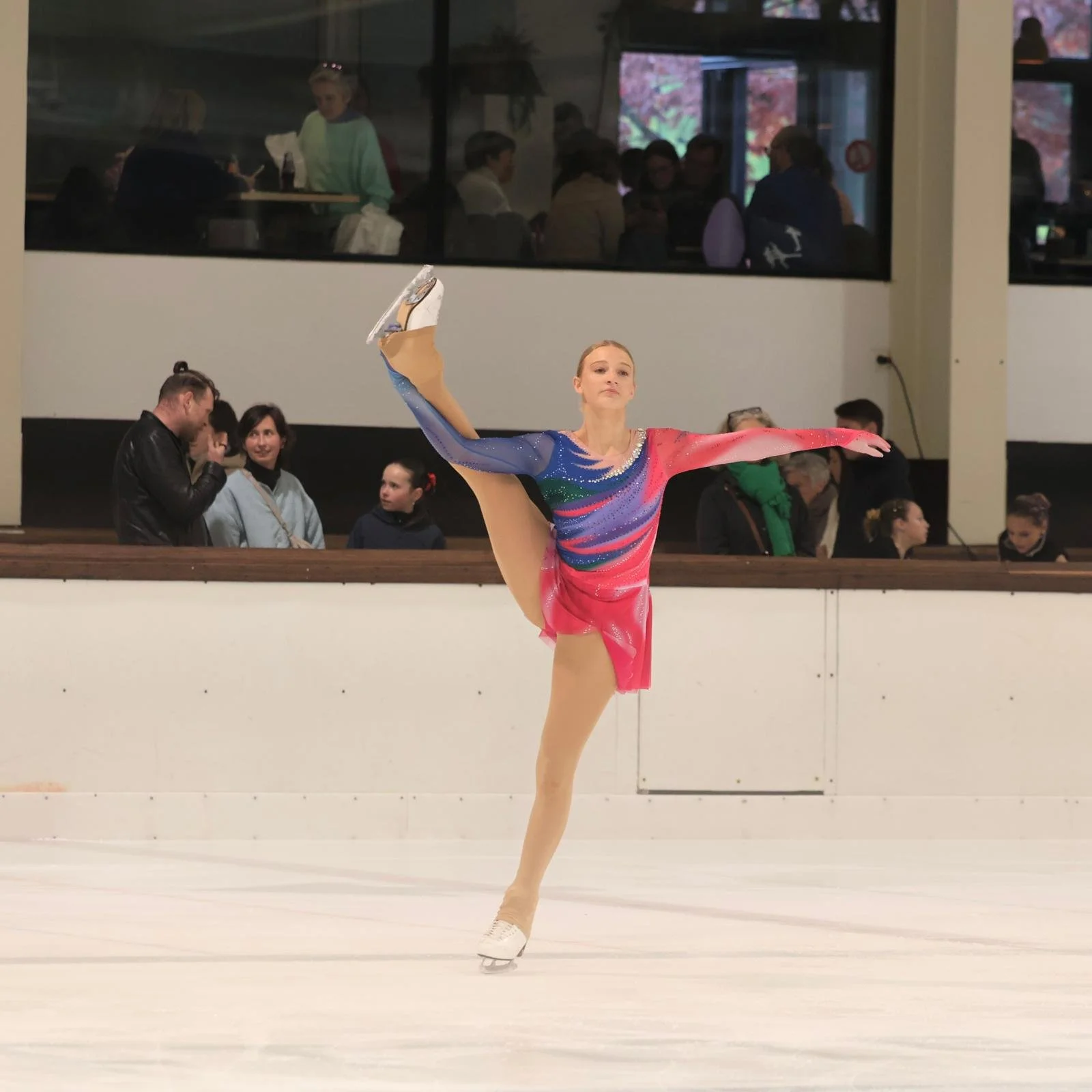 Schaatster in elegante pose met kleurrijk pakje in roze en blauwtinten van Atelier Nadja & Tutti Leotards