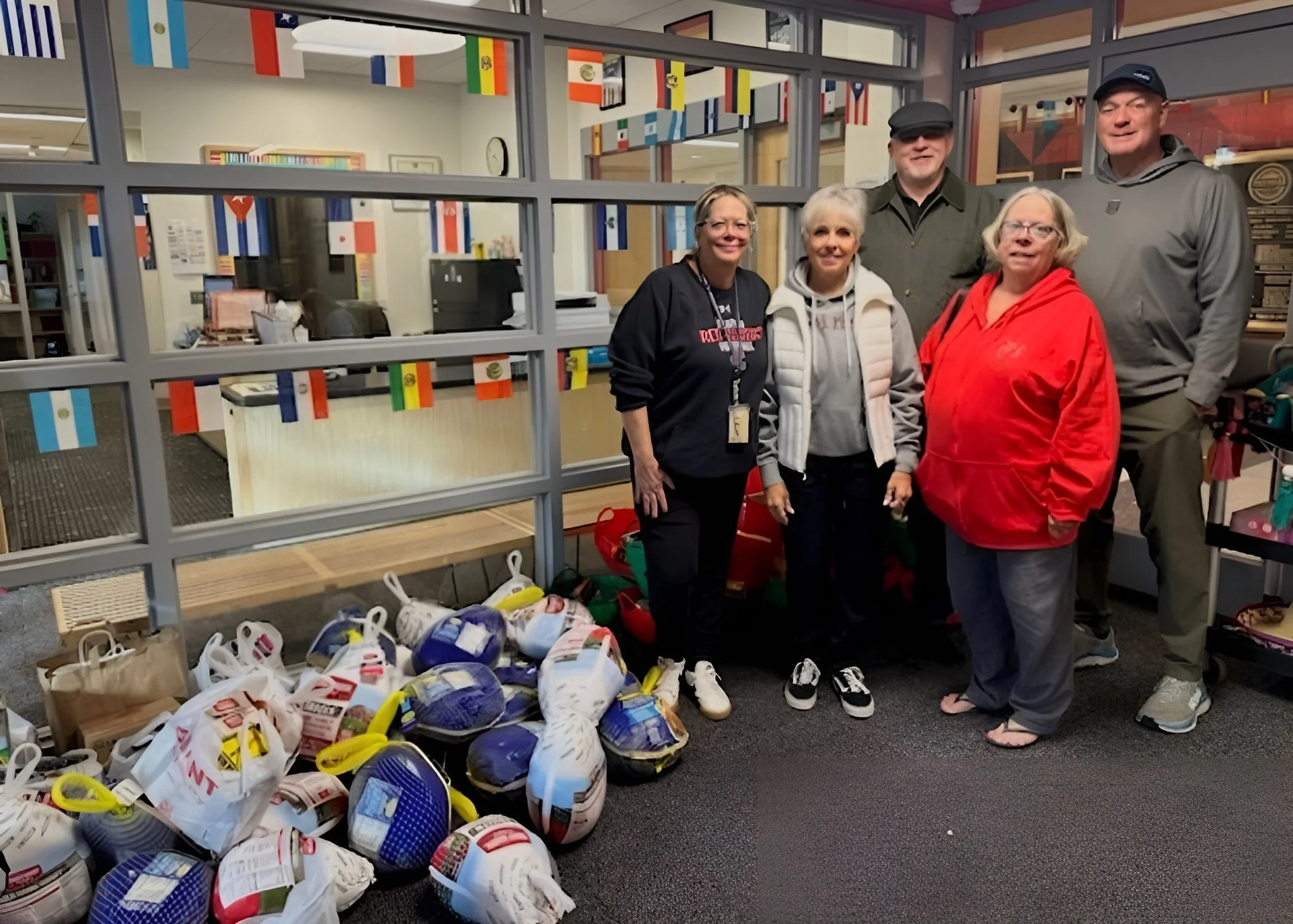 Group of five people standing inside a building with international flags hanging above. There are bags and shoes on the floor in front of them.