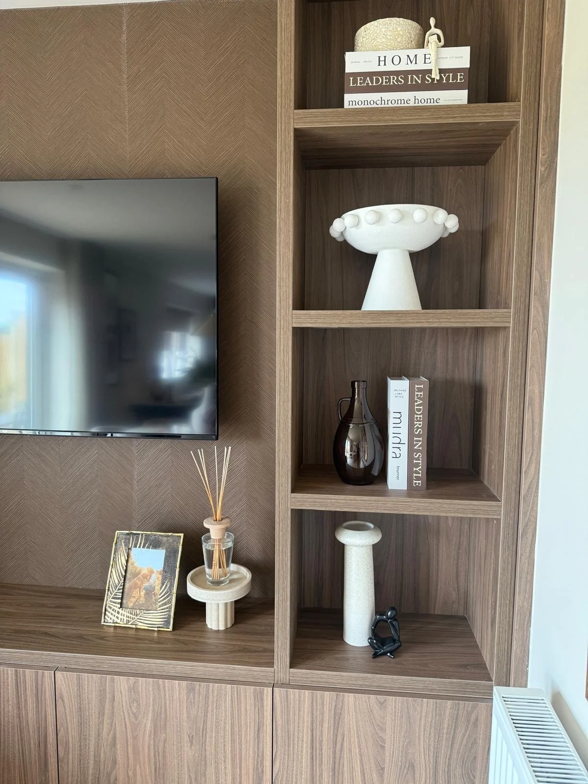 Bespoke wood-slat media wall with open shelving and styled travertine coffee table in a Colwyn Bay show home by The Design House