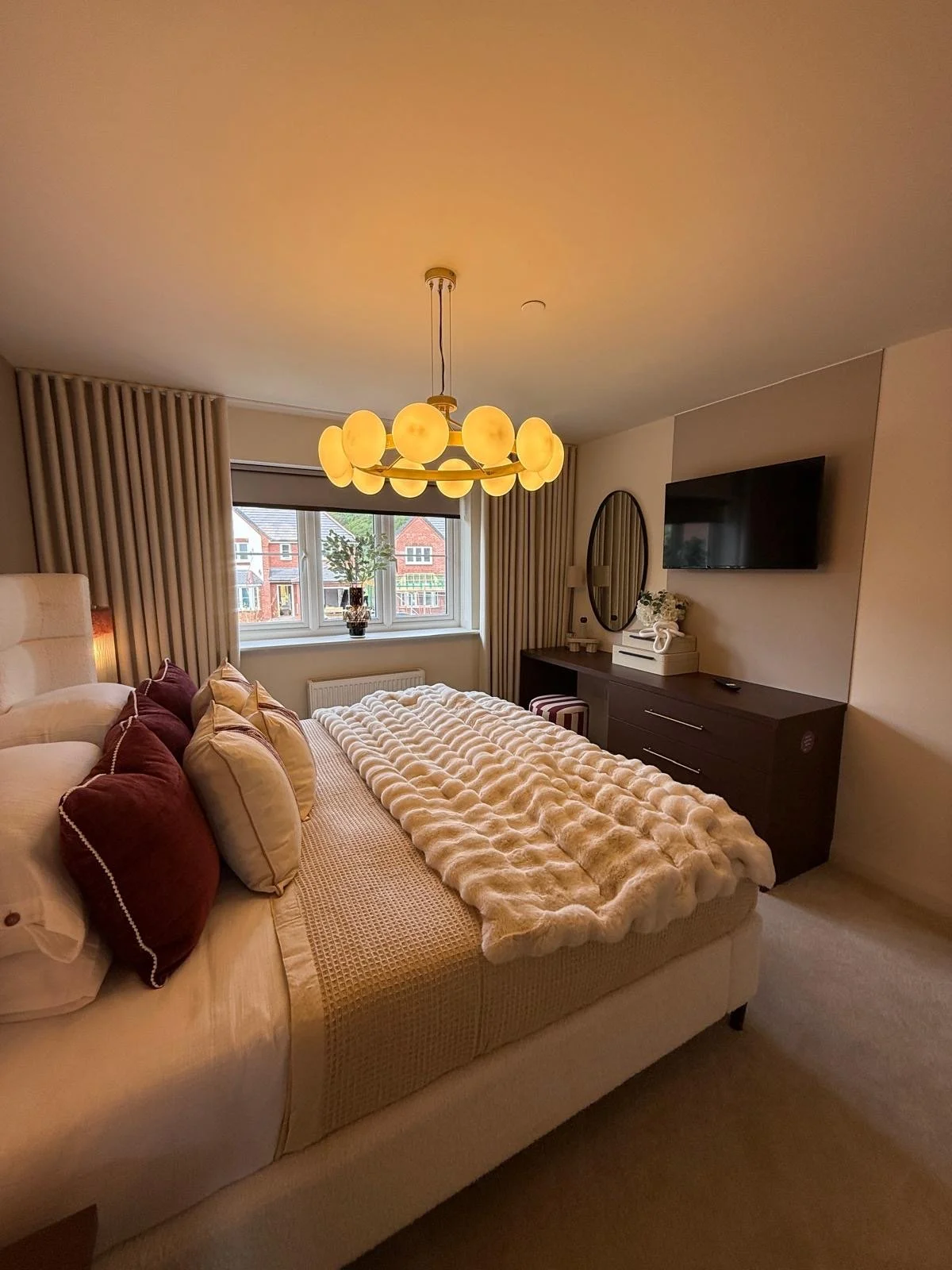 Show home principal bedroom at Hafan y Glyn, Colwyn Bay, with alabaster globe chandelier, wave curtains and layered cream and damson bedding