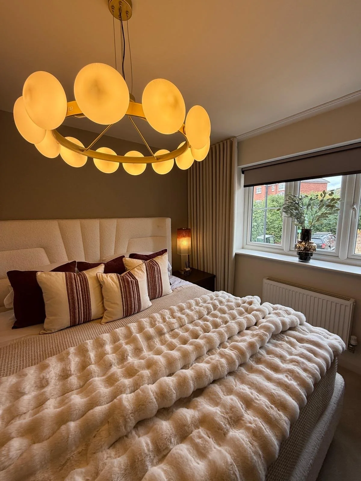 Show home principal bedroom at Hafan y Glyn, Colwyn Bay, with alabaster globe chandelier, wave curtains and layered cream and damson bedding