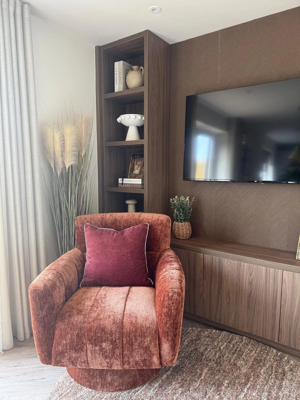 Rust velvet swivel chair beside bespoke walnut joinery and media wall in a show home designed for WPV Homes