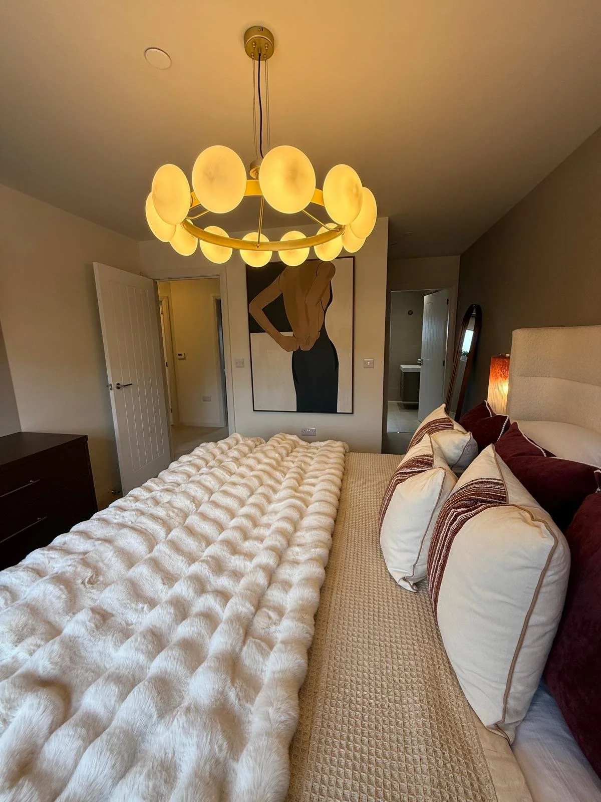 Show home principal bedroom at Hafan y Glyn, Colwyn Bay, with alabaster globe chandelier, wave curtains and layered cream and damson bedding