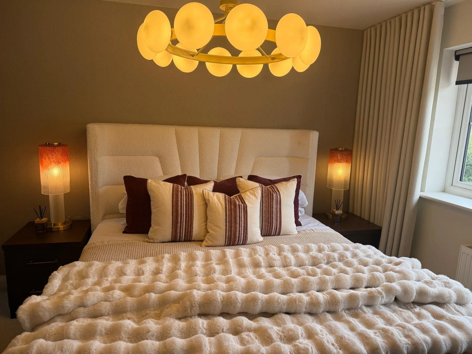Show home principal bedroom at Hafan y Glyn, Colwyn Bay, with alabaster globe chandelier, wave curtains and layered cream and damson bedding