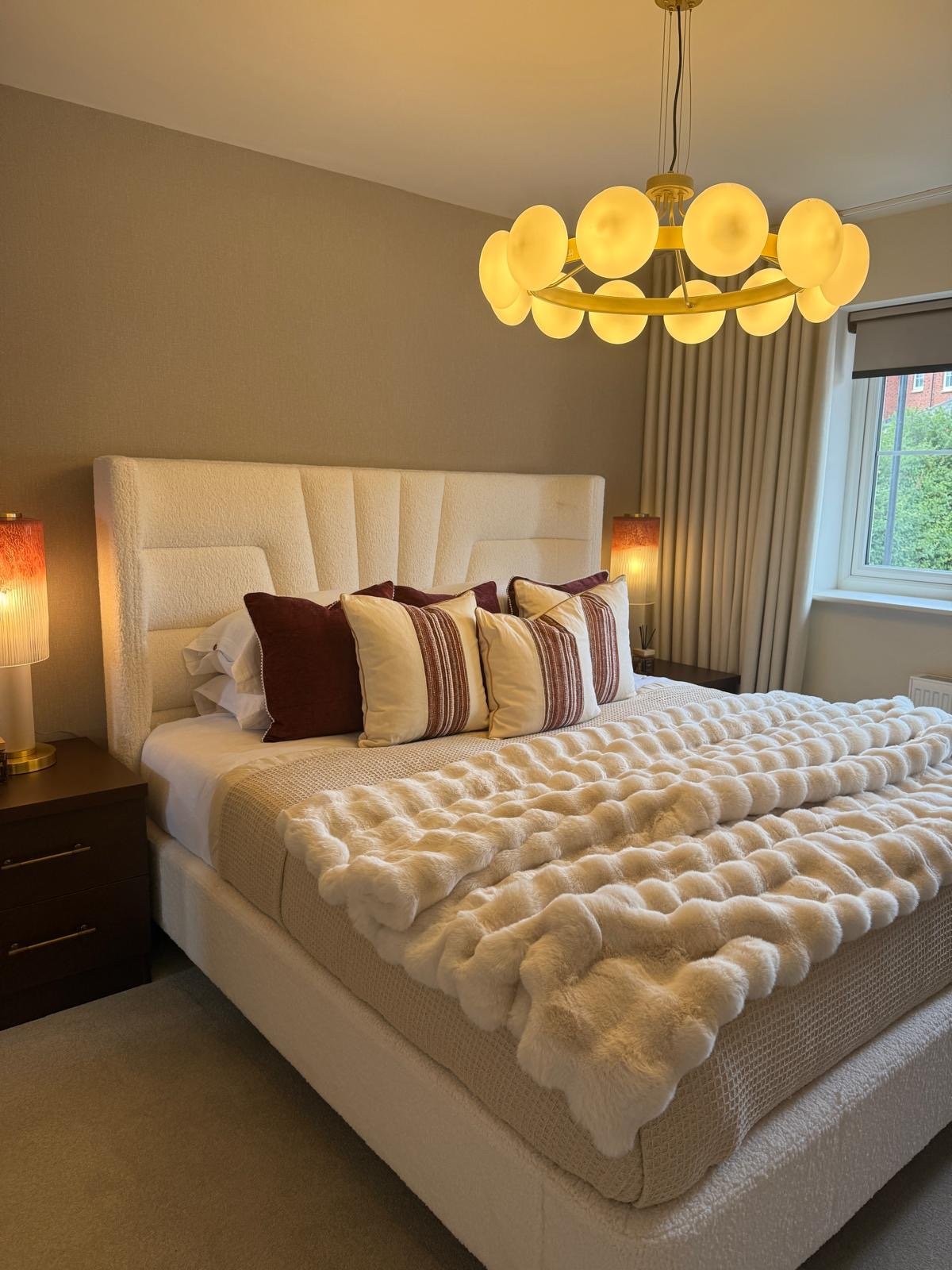 Show home principal bedroom at Hafan y Glyn, Colwyn Bay, with alabaster globe chandelier, wave curtains and layered cream and damson bedding